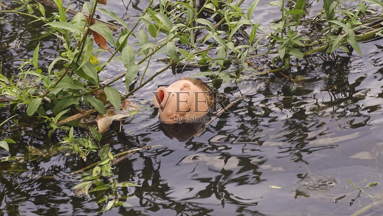 老娃娃的头被丢弃在地上的水坑里。特写镜头。照片摄影图片