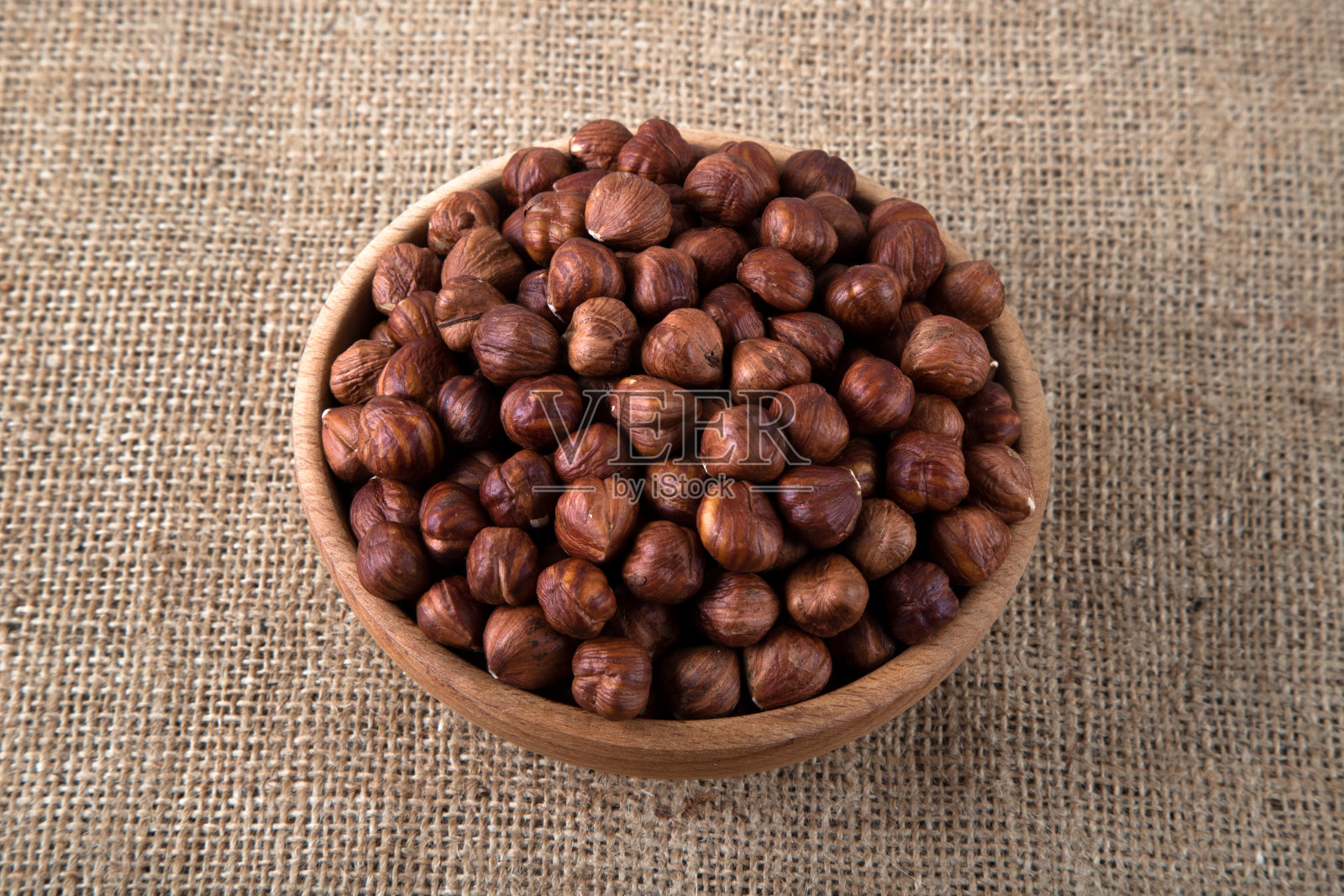 一碗剥了皮的榛子放在粗麻袋上，俯视图照片摄影图片