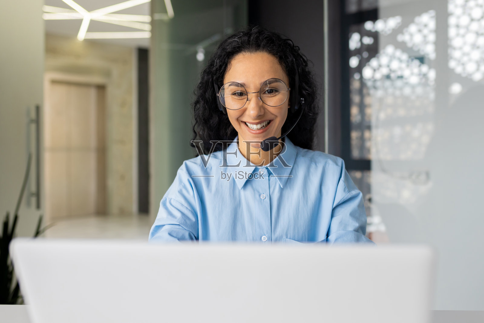 年轻漂亮的女人在办公室使用视频通话耳机工作，西班牙裔在线客服人员在笔记本电脑上打字照片摄影图片