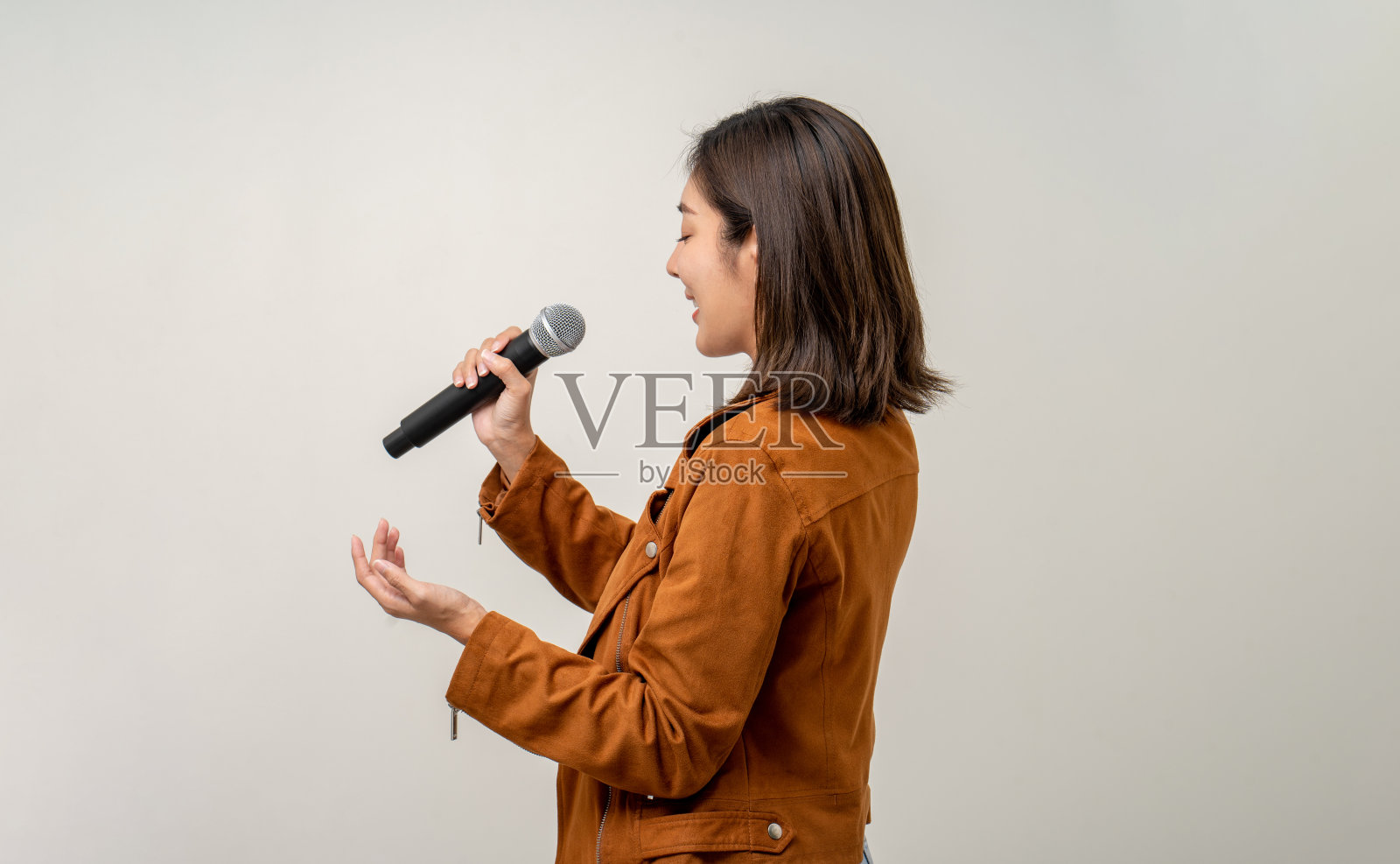 快乐年轻的亚洲女人唱歌。孤立背景的艺术家兼歌手。自信的女性在演播室拿着麦克风公开演讲。照片摄影图片