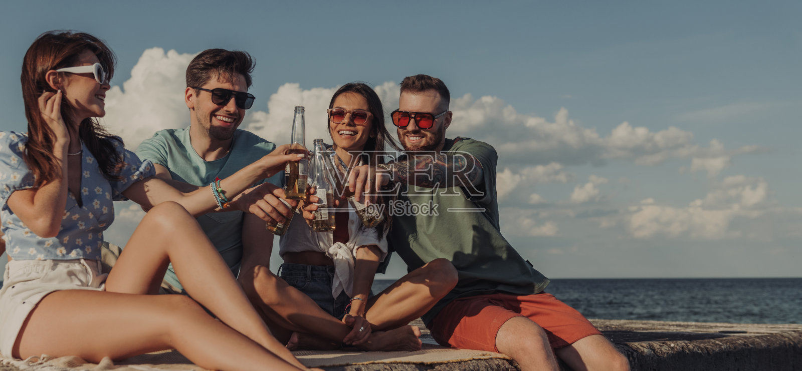 一群快乐的年轻朋友在海边喝着啤酒，一起度过无忧无虑的时光照片摄影图片