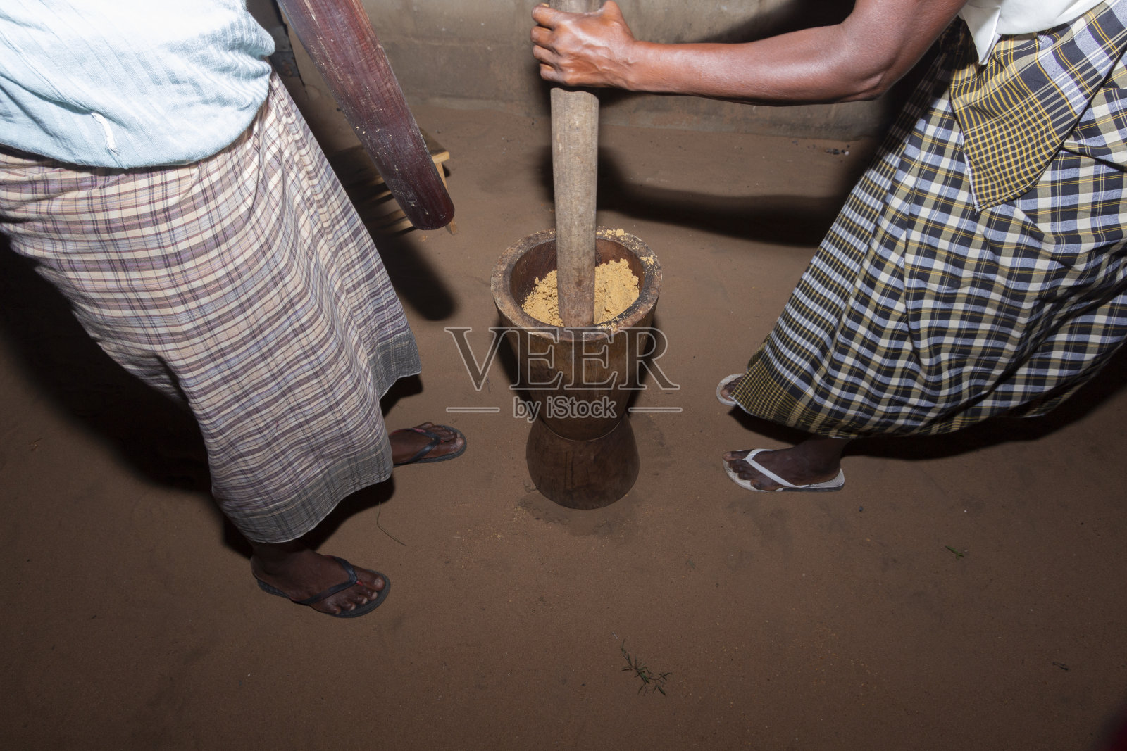 妇女们晚上在一个非洲传统的大木臼里捣花生和木薯粉照片摄影图片