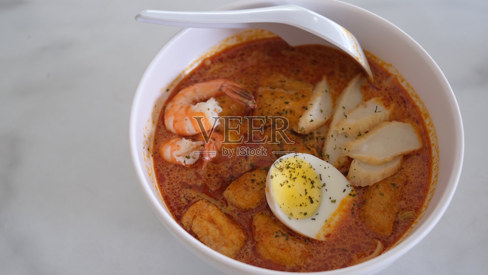 白色桌子上的白色碗里盛着新加坡叻沙。新加坡的食物。照片摄影图片