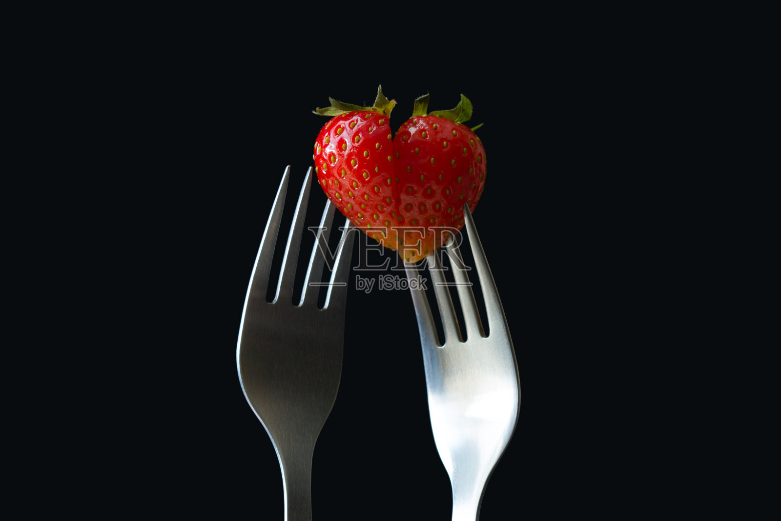 两个相互匹配的一半心形草莓在叉子上黑色的背景照片摄影图片