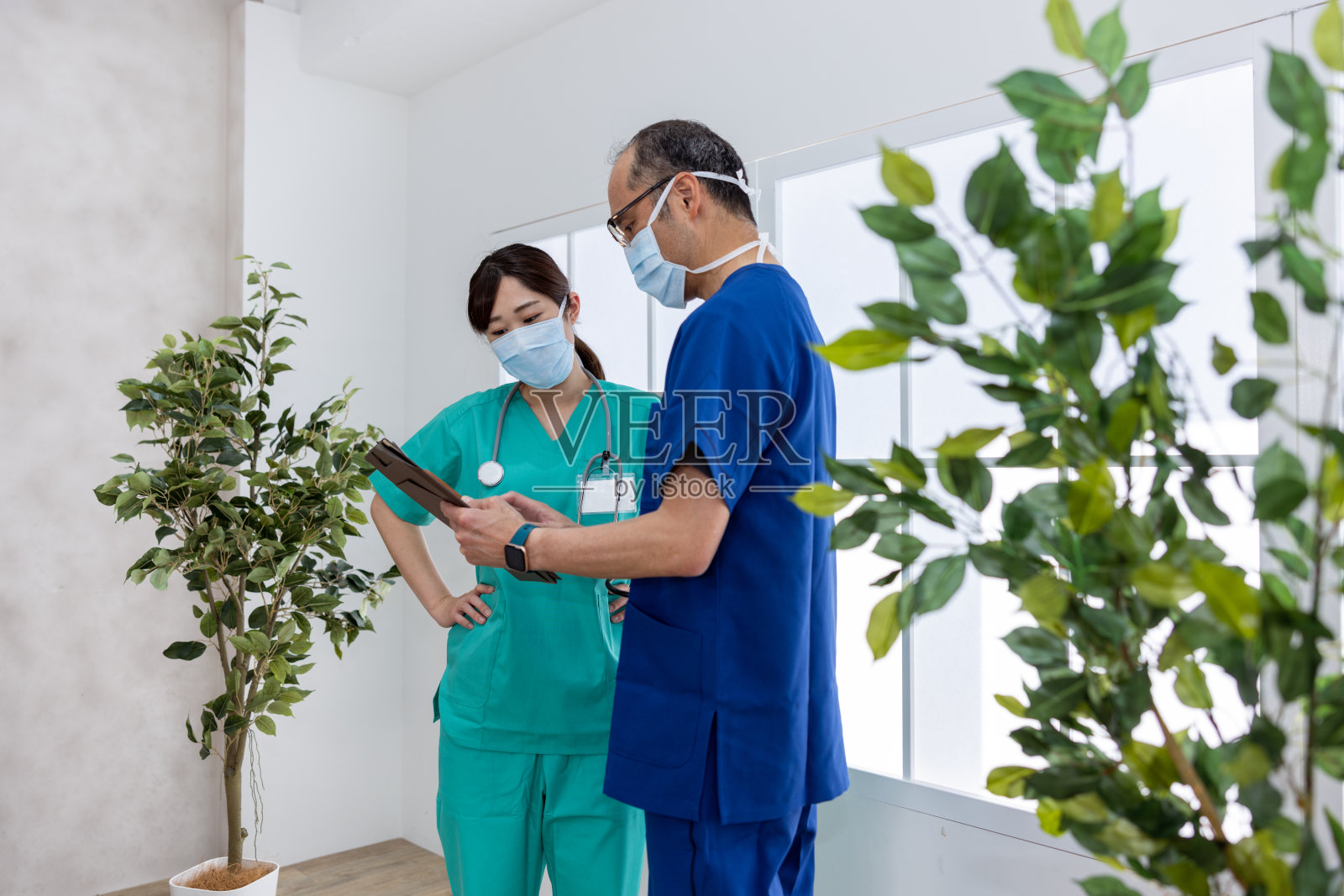 男医生和女医生都戴着医用棉衣和医用口罩在医院讨论——手放在臀部上照片摄影图片