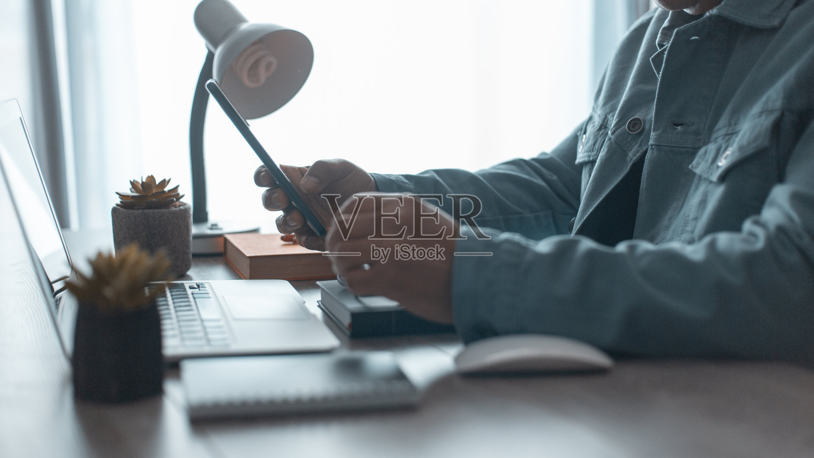 休闲商务人士使用移动智能手机和笔记本电脑，在家庭办公室桌上的记事本上写字，男人在提醒计划上做笔记照片摄影图片