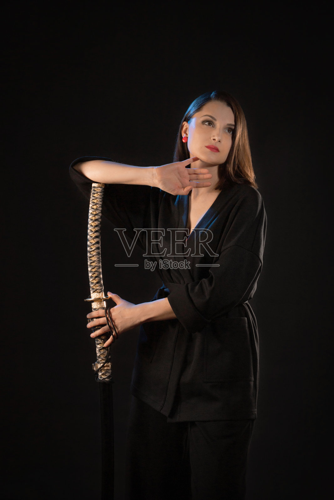一个沉思的年轻黑发女人的垂直肖像与武士刀在黑色的背景照片摄影图片