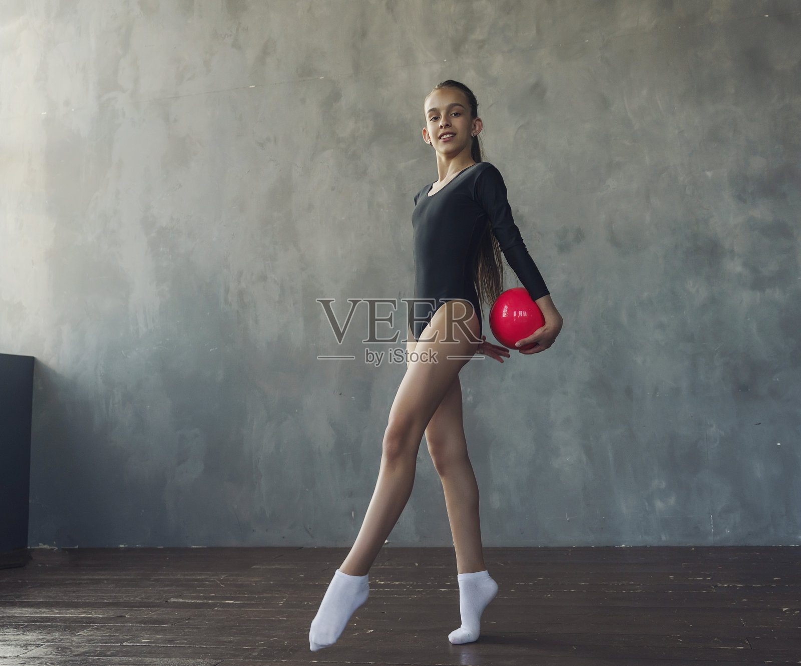 一个年轻的艺术体操女孩穿着黑色的运动服，拿着球做体操练习照片摄影图片