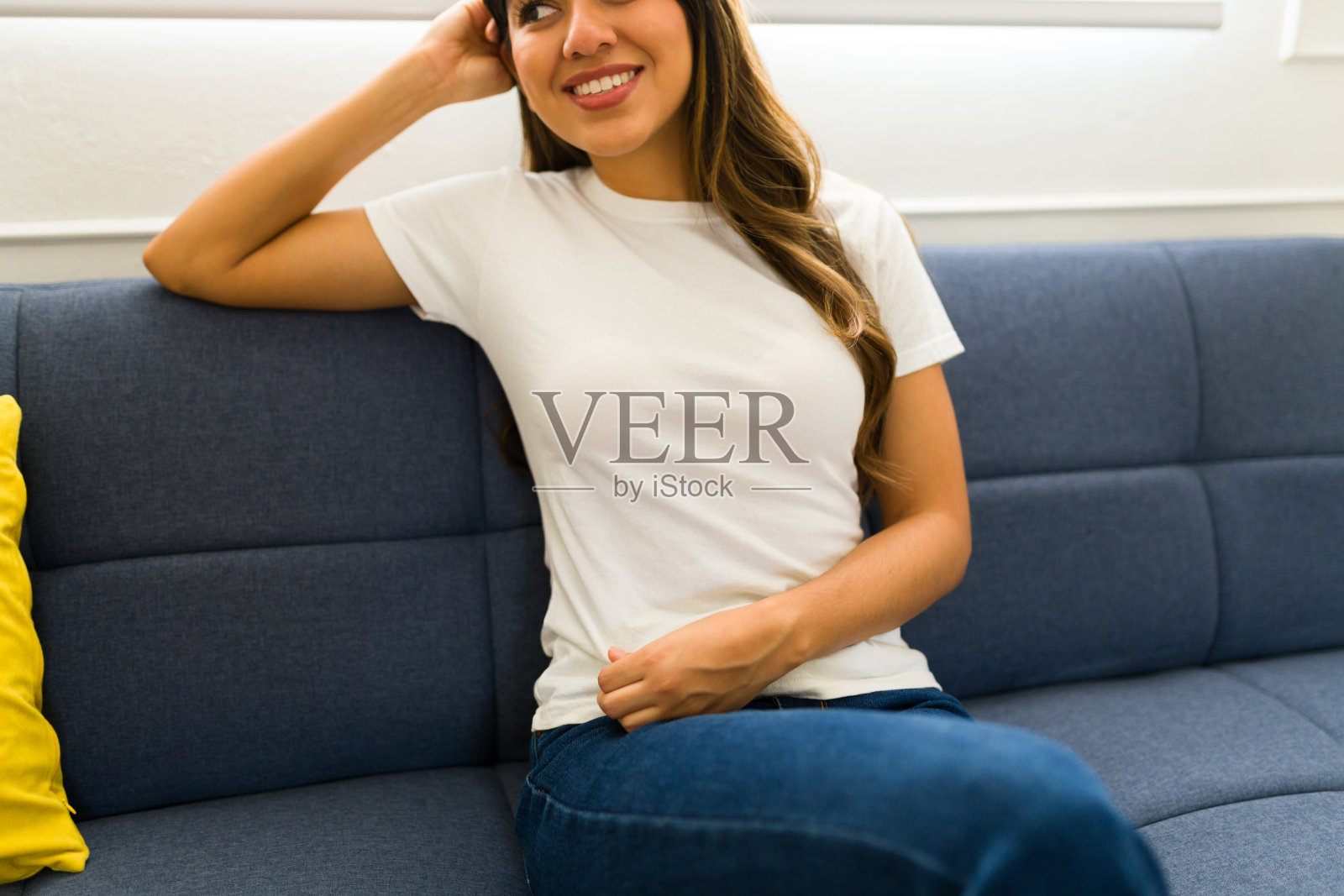 一个微笑的女人坐在沙发上，穿着一件白色的模拟t恤照片摄影图片