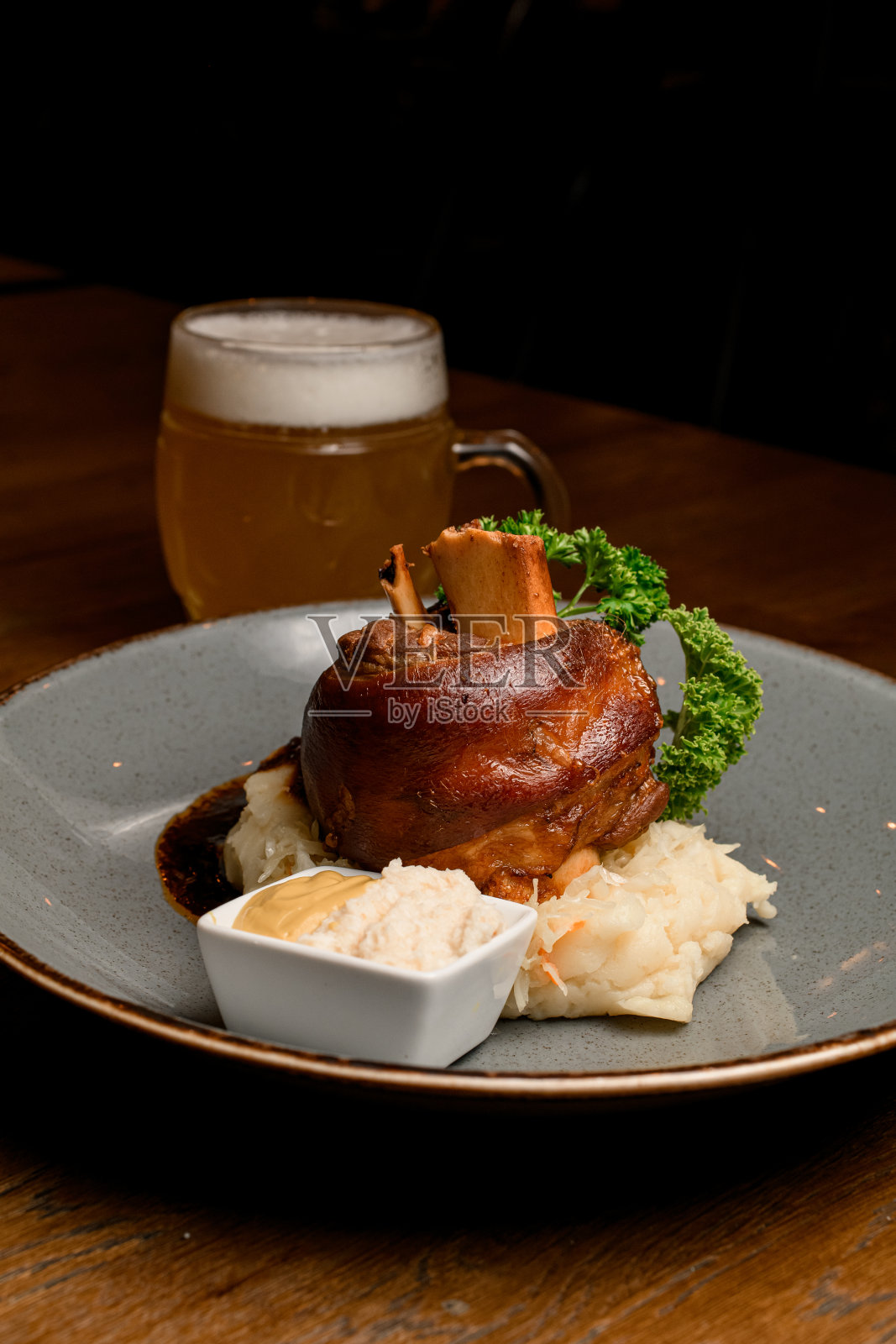 煎猪蹄配上香草和酱汁，在盘子里放上一杯啤酒照片摄影图片