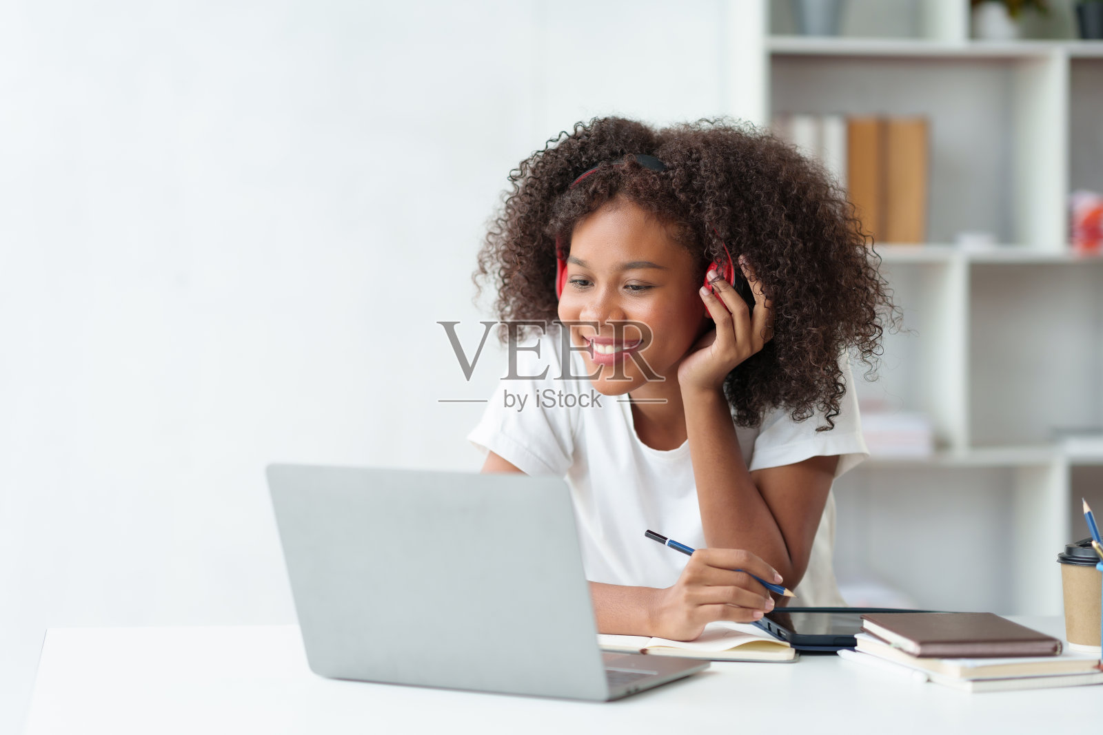 漂亮的年轻女学生戴着耳机在笔记本电脑上视频聊天，笑脸和手势愉快地学习。照片摄影图片