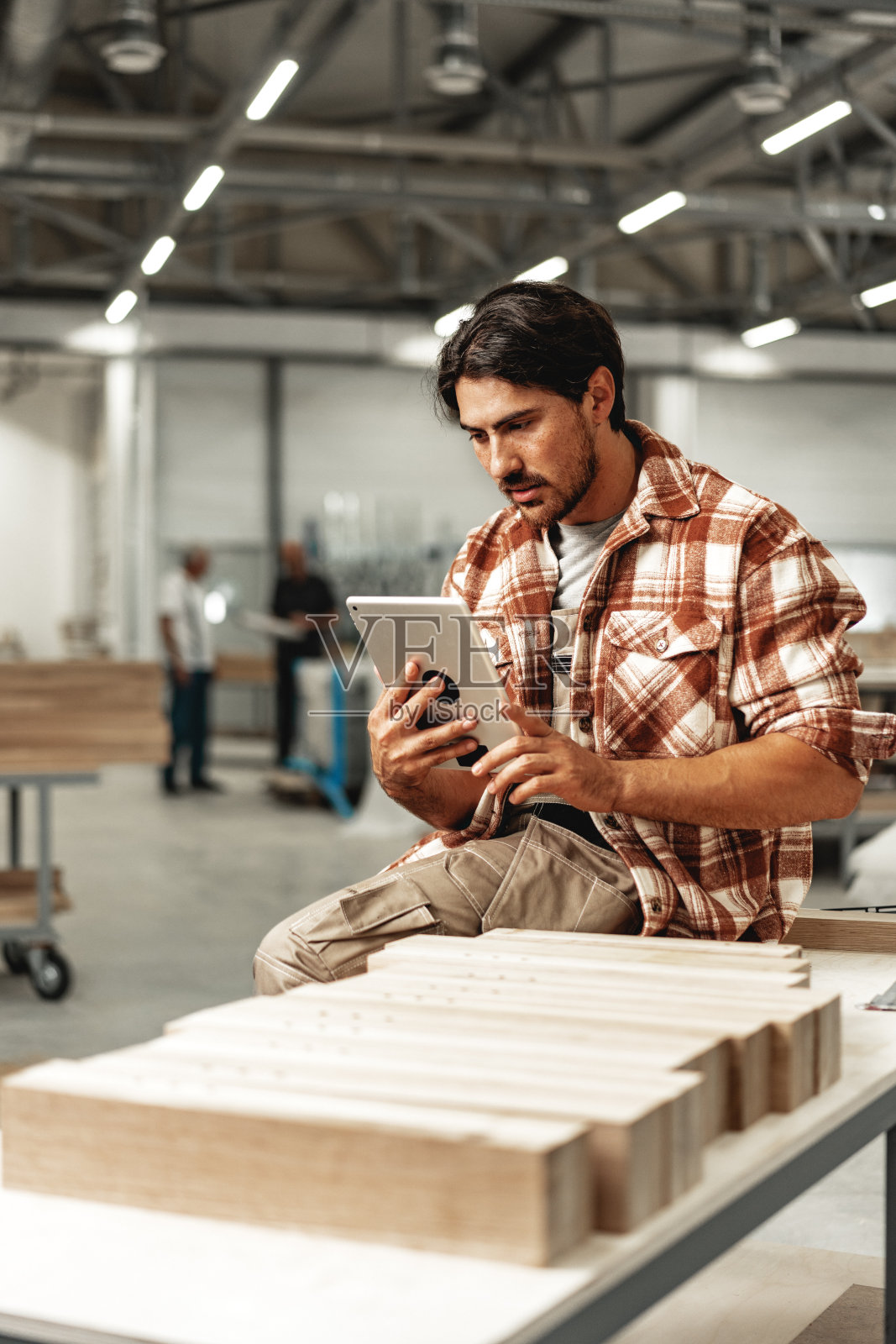 年轻的木匠站在他的车间里使用数码平板电脑照片摄影图片