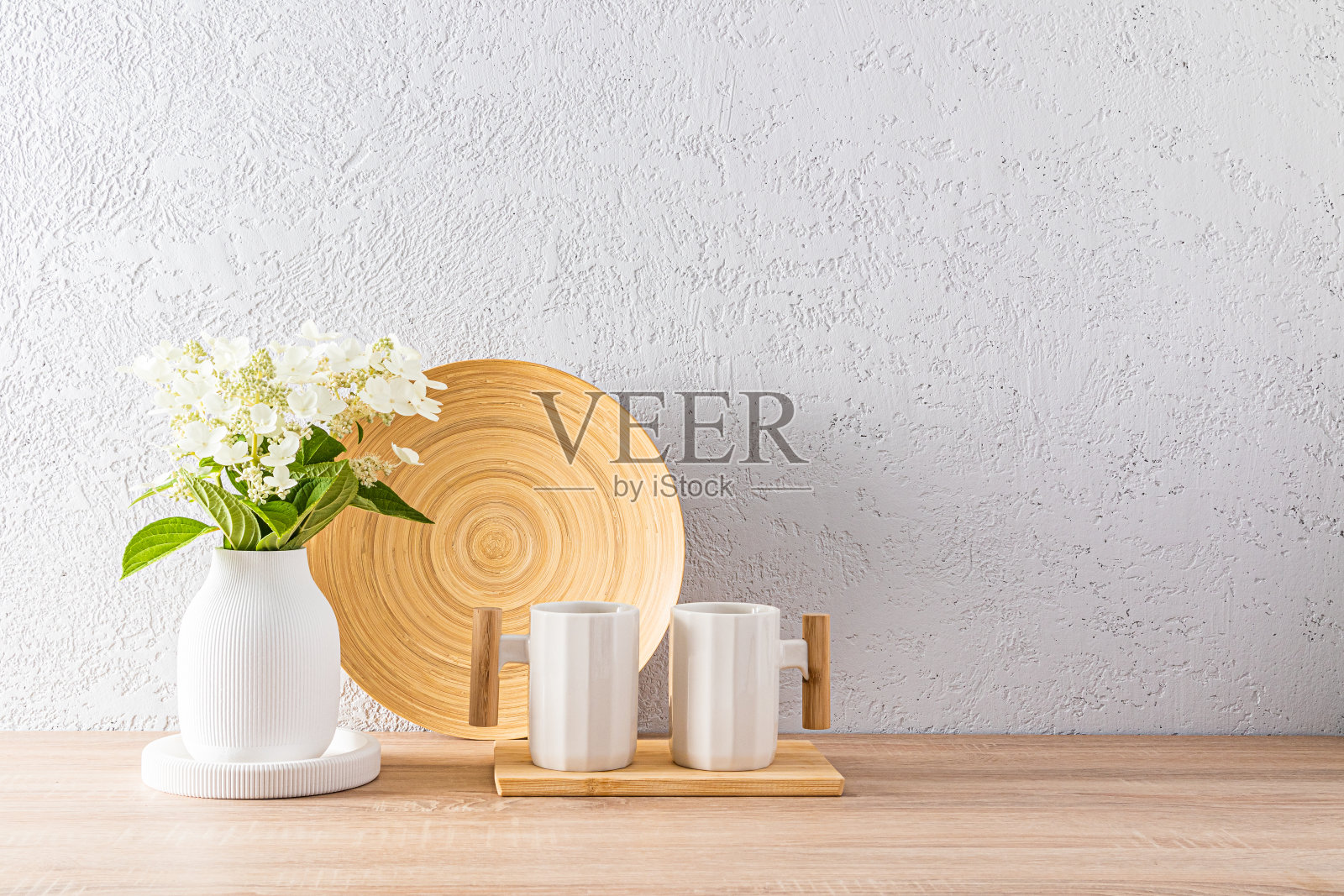 两个时髦的木制把手白色陶瓷马克杯，放在现代的台面上，厨房内部有一个浅色的花瓶和一个盘子。Eco的风格。照片摄影图片
