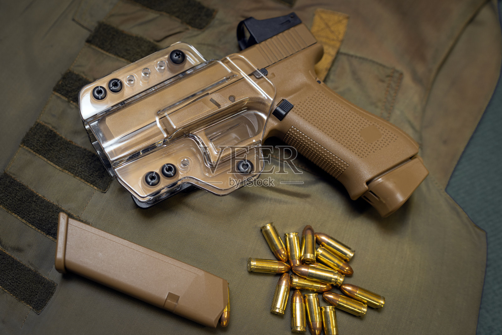 沙色手枪，装在透明的枪套里，背景是迷彩防弹衣上的弹匣和子弹照片摄影图片