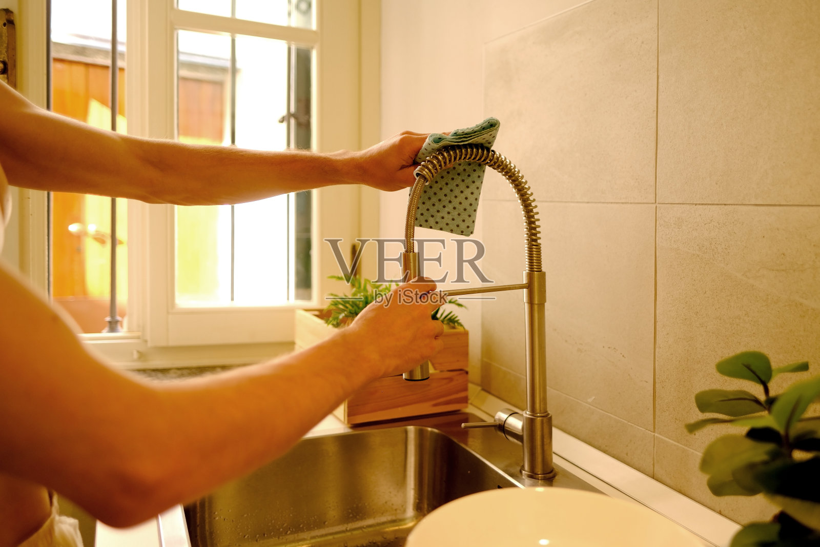 特写男性双手用湿布清洁厨房，清洁镀铬水槽龙头，现代家政，保持生活空间整洁照片摄影图片