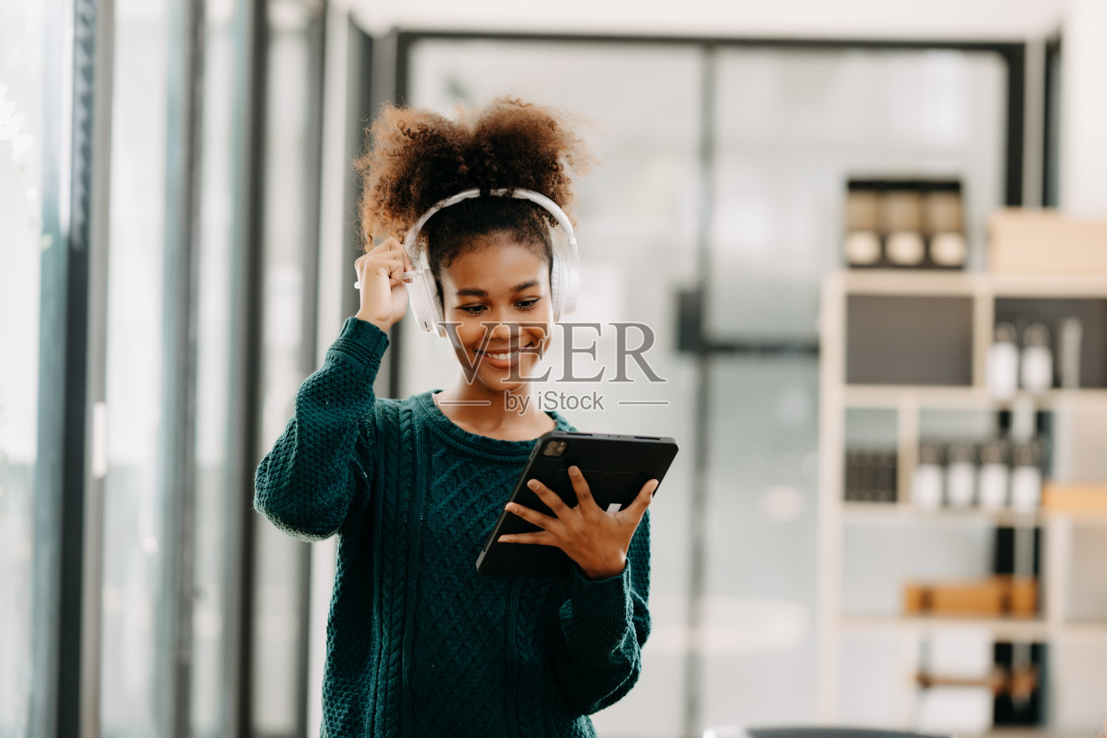 迷人的年轻非洲学生在大学图书馆学习，坐在书桌前，使用笔记本电脑，平板电脑和耳机进行视频聊天。照片摄影图片