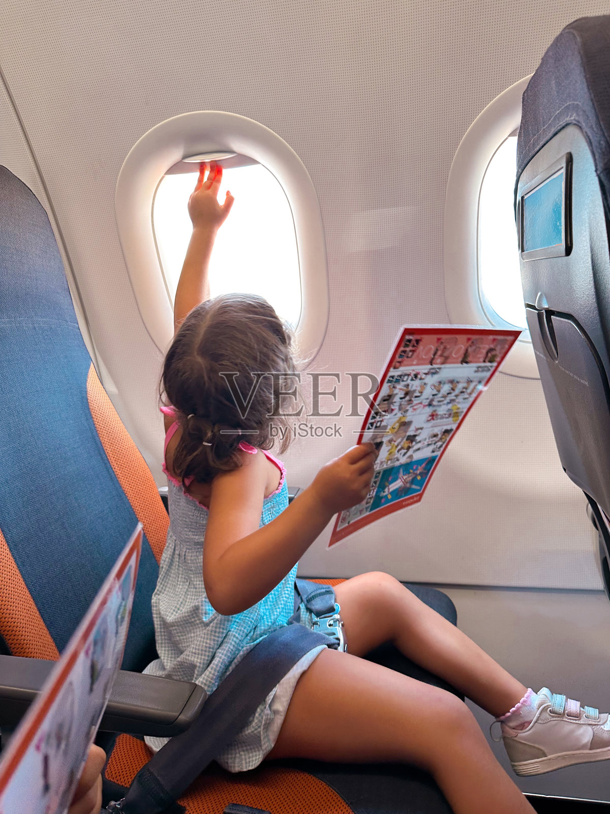 在葡萄牙，一个小女孩手里拿着安全须知，关上了飞机窗户照片摄影图片
