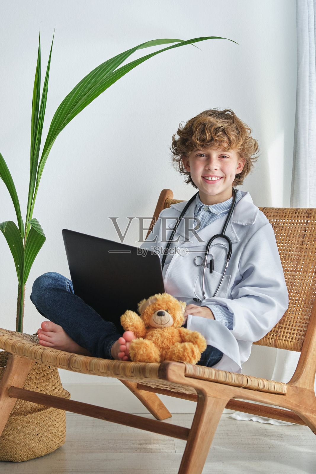 快乐的男孩医生带着笔记本电脑和椅子上的软熊照片摄影图片