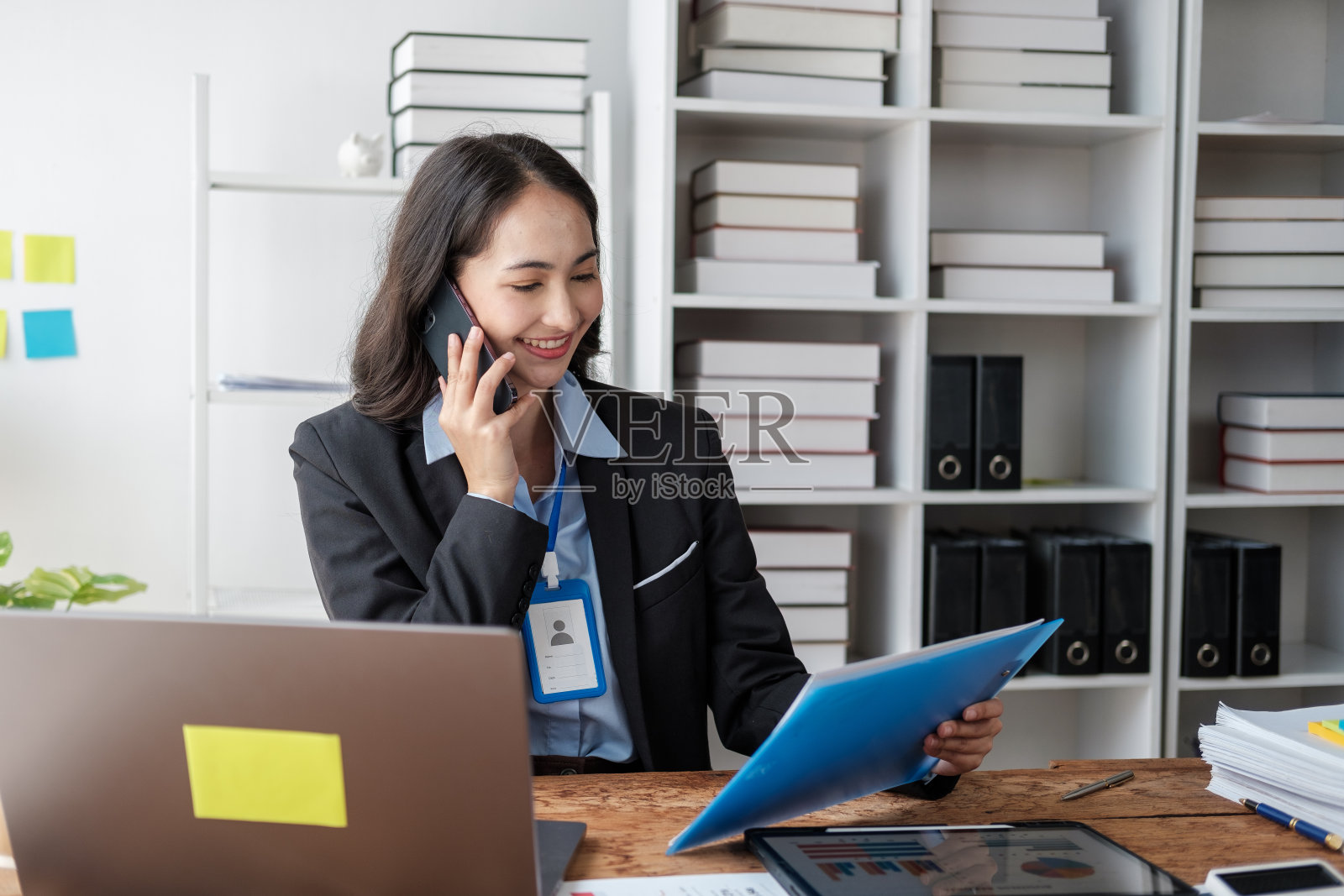 在办公室用智能手机微笑的年轻亚洲女商人。照片摄影图片