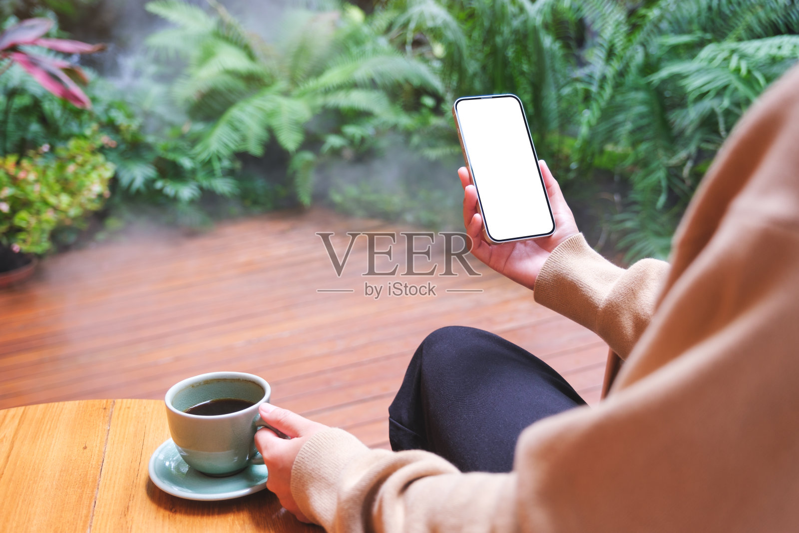 一个女人在花园里喝咖啡，拿着空白桌面屏幕的手机的模型图照片摄影图片