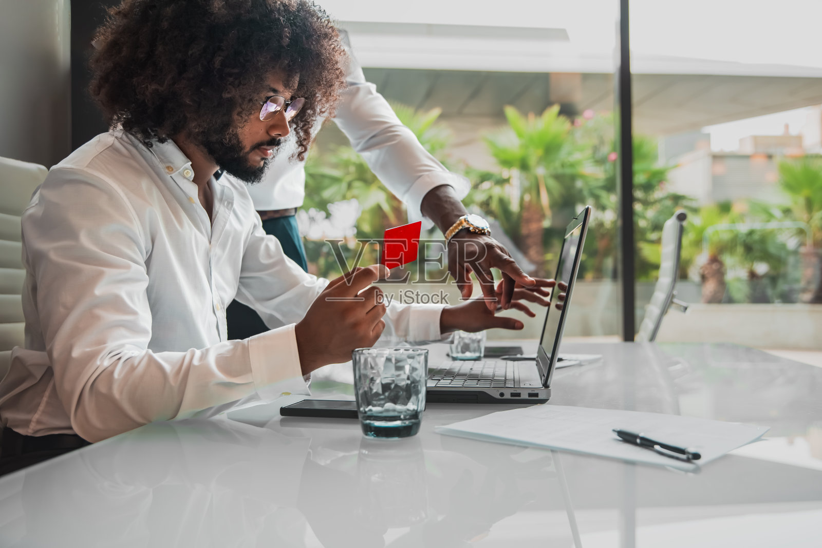 这位商人拿着信用卡，在办公室用笔记本电脑进行网上支付。照片摄影图片