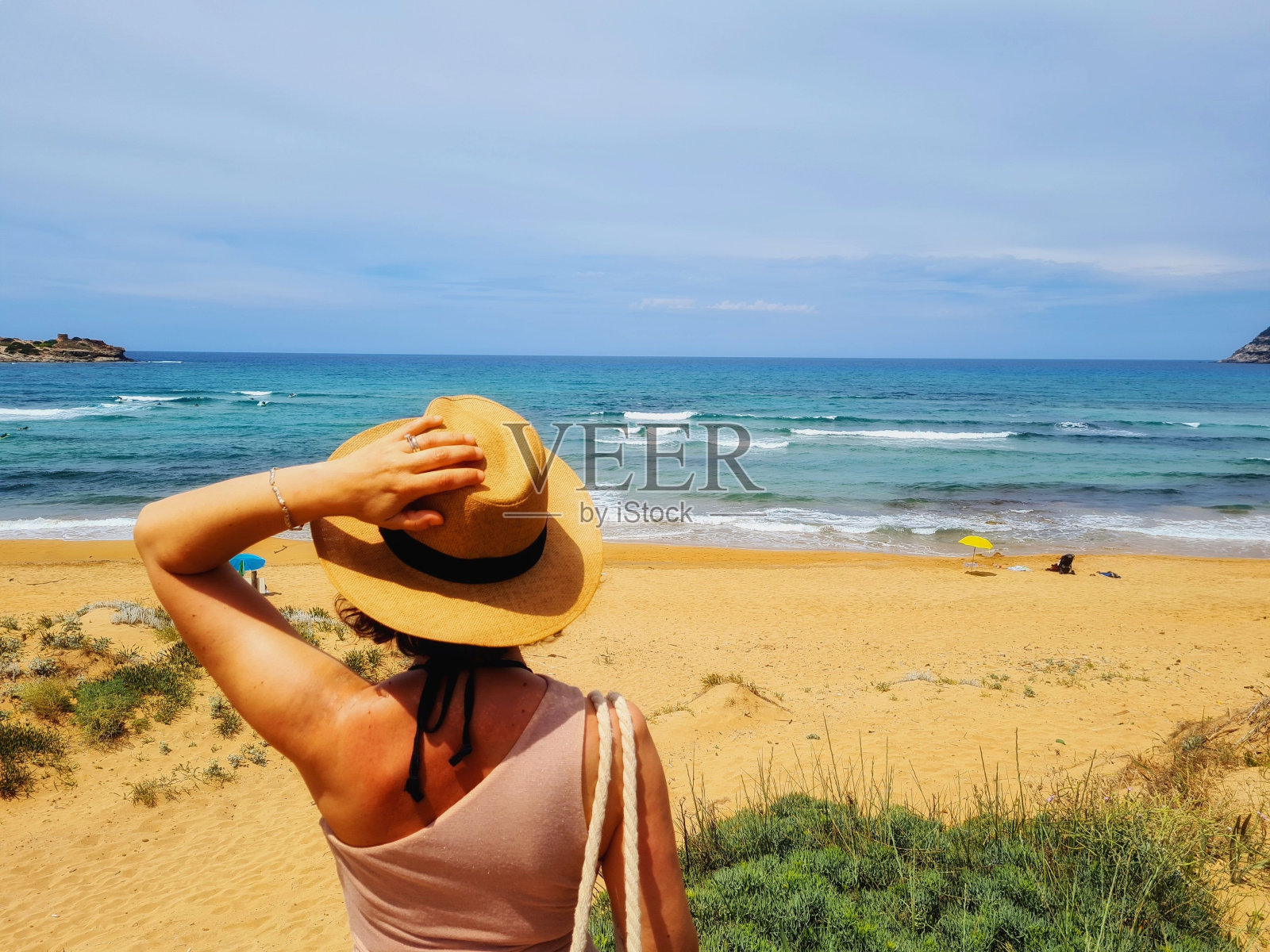 拿着一根稻草的女人站在海滩上俯瞰大海照片摄影图片