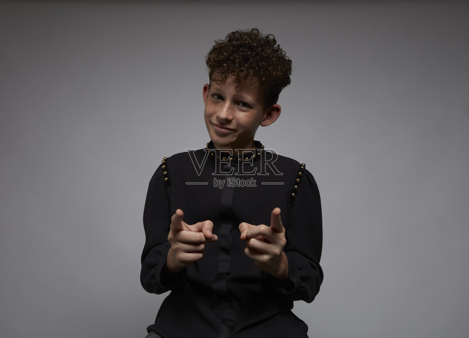 一个长着雀斑和卷发的小男孩指着镜头，摆出一副自信的姿势。照片摄影图片