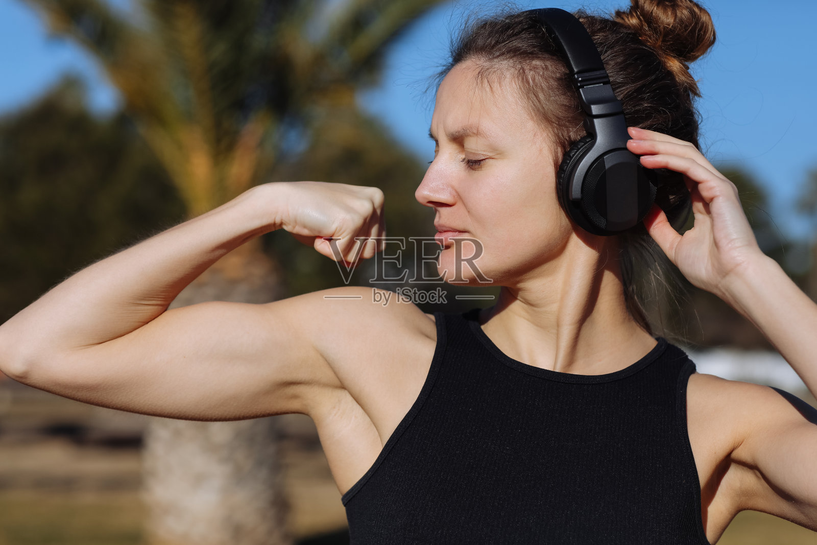 穿着运动服的年轻美女举起双臂，露出肌肉、二头肌，展示强壮的手，在户外有苗条的身材，对胜利充满信心，看起来独立，微笑积极照片摄影图片