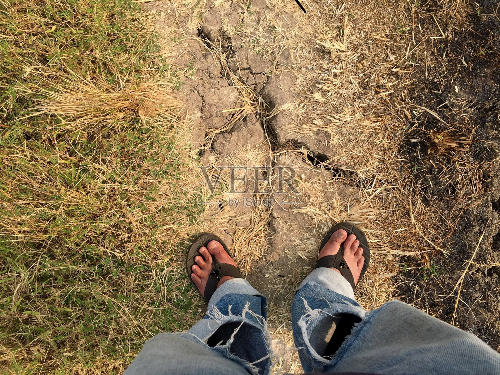 穿着凉鞋的脚穿着破旧的牛仔裤站在地上照片摄影图片