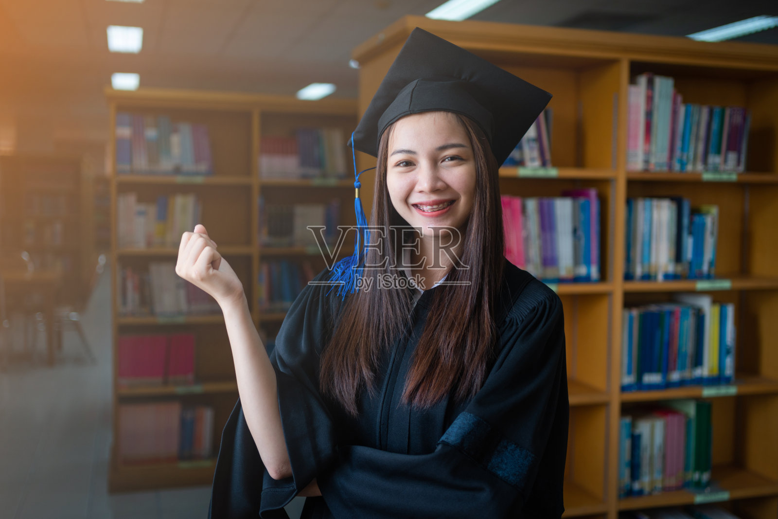 一名亚洲女大学毕业生穿着毕业礼服在大学图书馆庆祝她的学位成就照片摄影图片