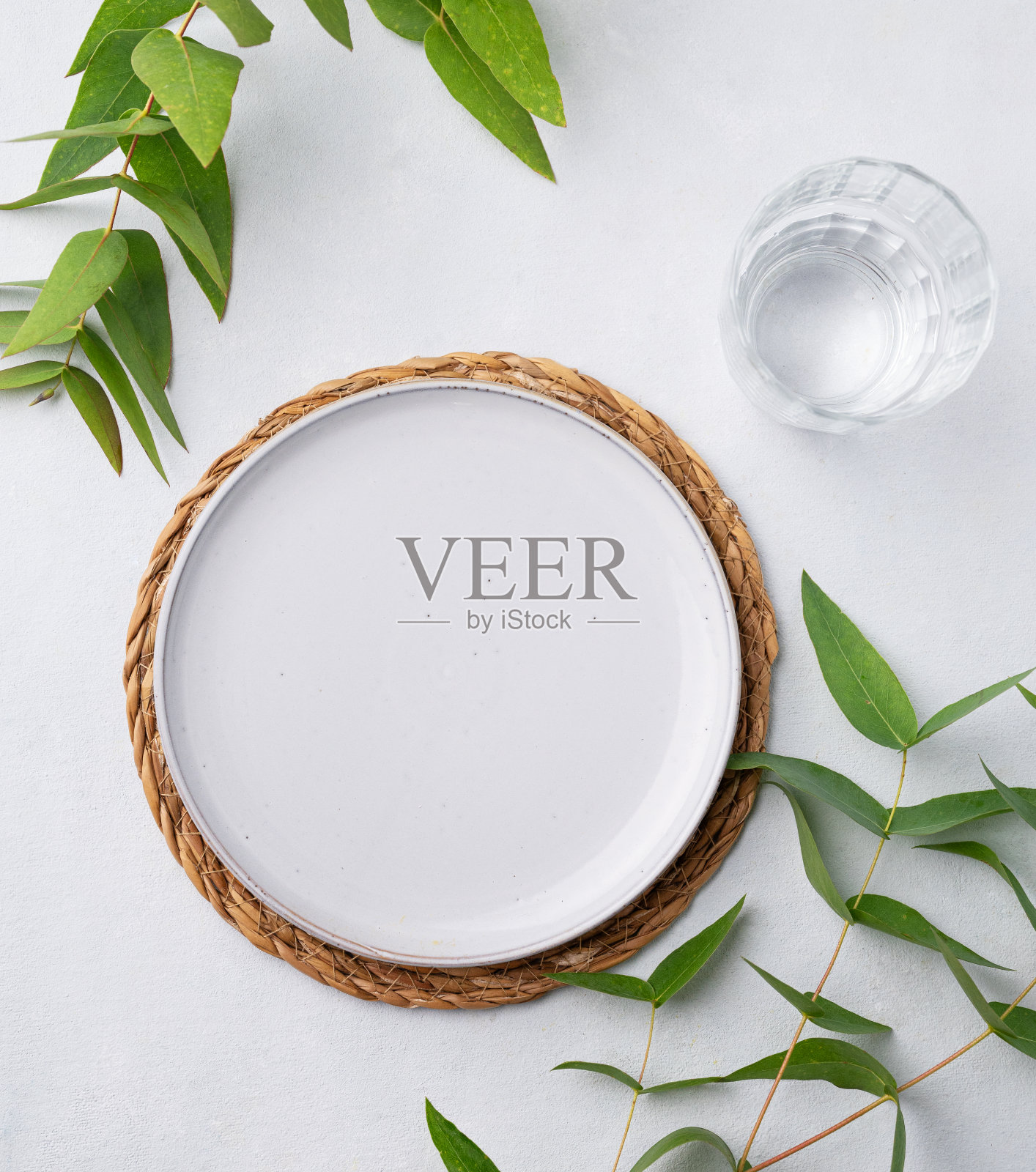 餐桌上有一个蓝色的盘子和一个杯子，放在一张稻草餐巾上，背景是浅色的桉树树枝。春天的餐具概念。照片摄影图片