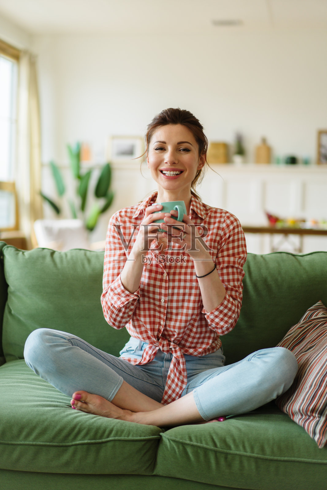 快乐的年轻女子坐在家里的沙发上。这个女人正在喝茶。照片摄影图片
