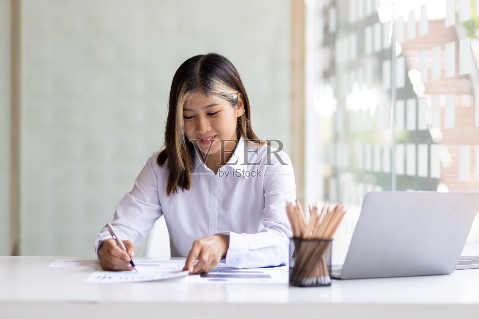 用笔记本电脑工作的女性，在办公桌上阅读商业财务报告文件。照片摄影图片