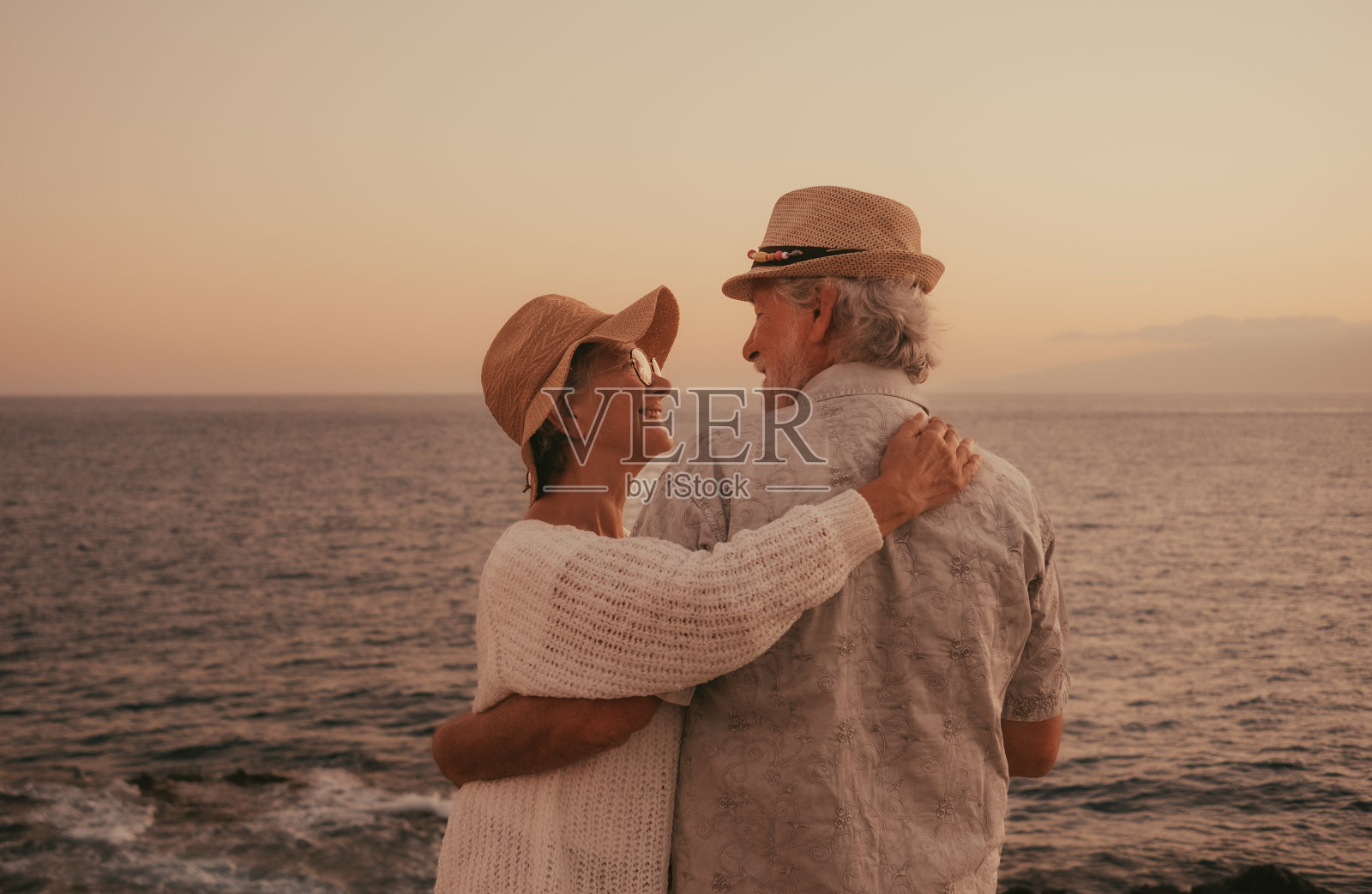 可爱的老年家庭夫妇拥抱着大海，深情地看着对方的眼睛。享受假期或退休生活的老年退休男女照片摄影图片