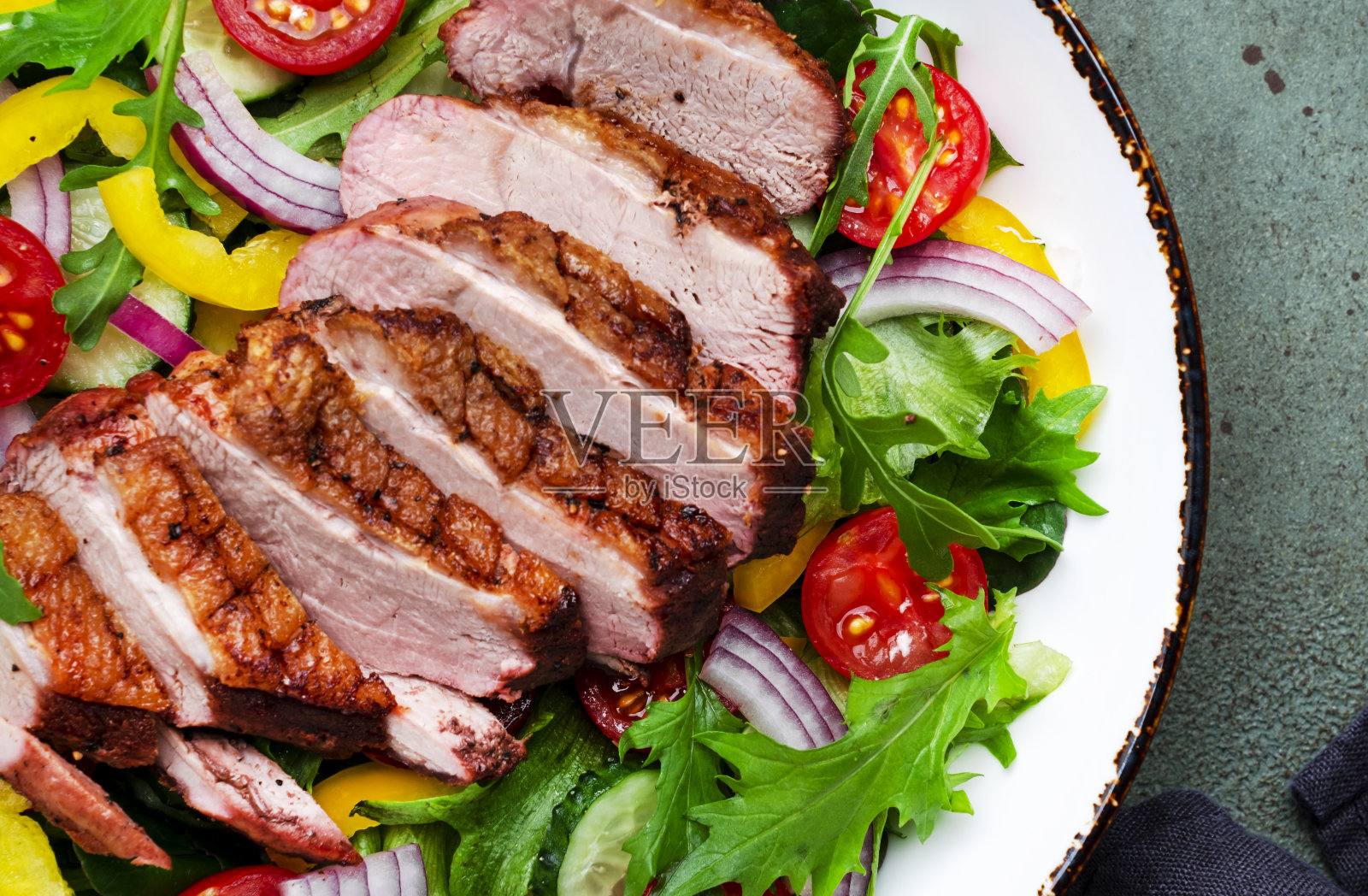 在绿色的餐桌背景上，用烤鸭胸片和圣女果、黄瓜、辣椒粉、红洋葱、生菜和芝麻菜做成的沙拉，俯视图照片摄影图片