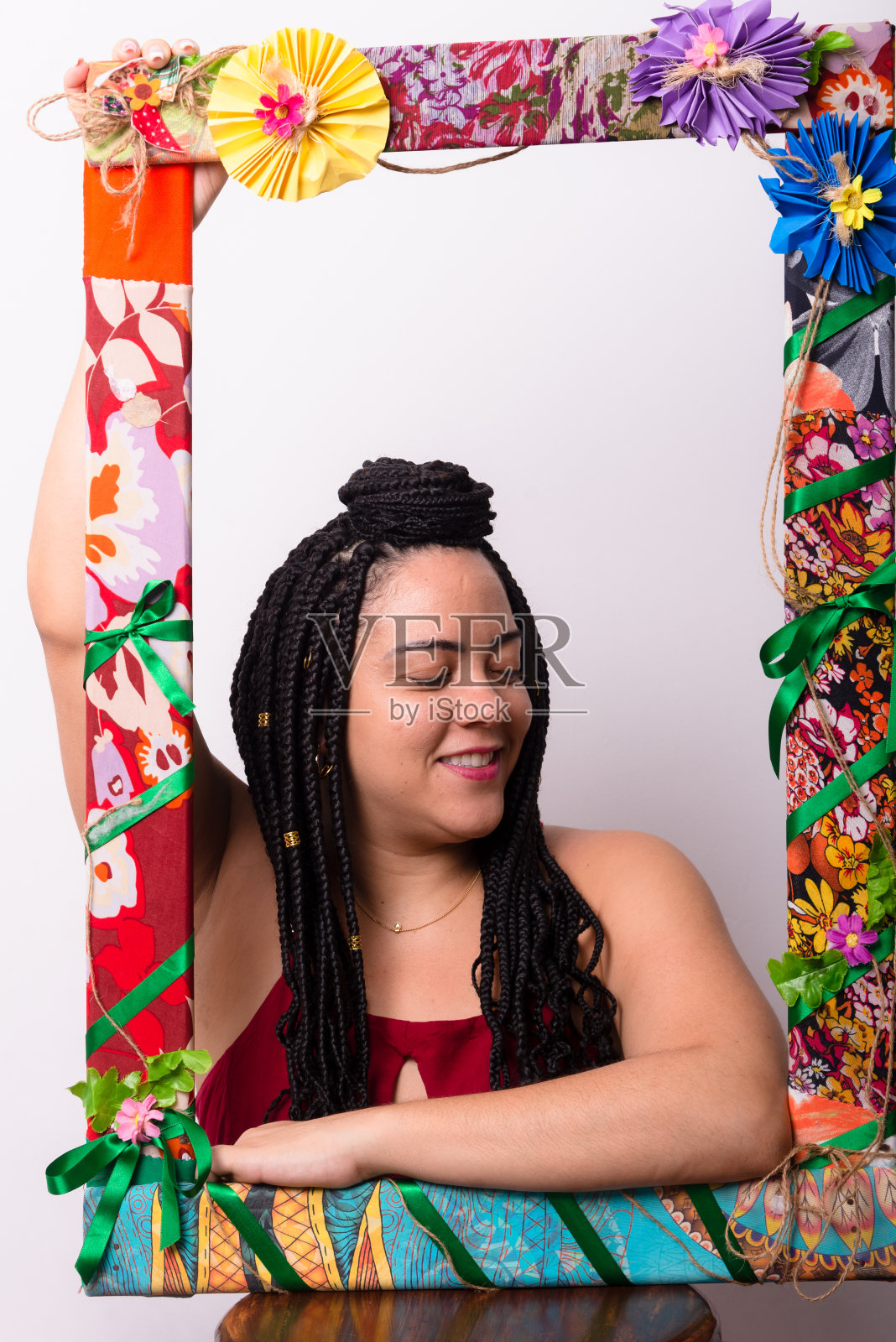 一个美丽的女人站在一个装饰着鲜花和五颜六色的衣服的框架后面。白色背景。照片摄影图片