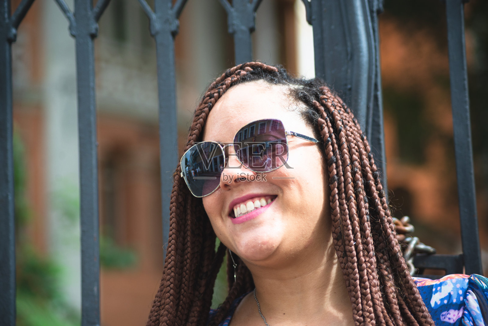 一个梳着辫子戴着墨镜靠在铁栏杆上的漂亮女人。照片摄影图片