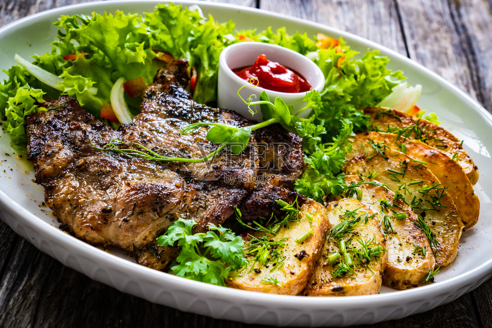 木桌上的烤猪颈、炸土豆片和新鲜蔬菜沙拉照片摄影图片