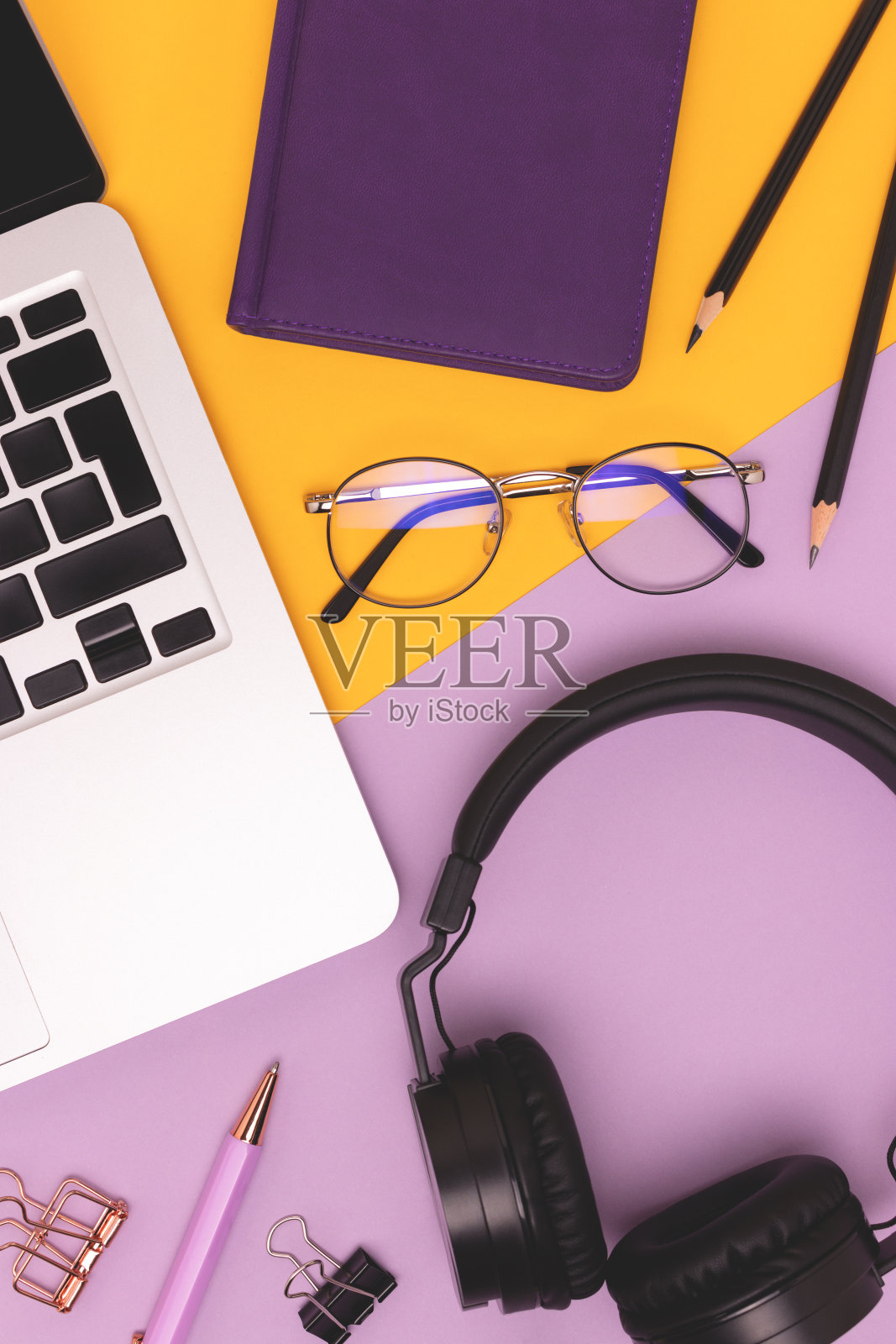 笔记本电脑，耳机和办公用品在紫色和黄色的背景。照片摄影图片