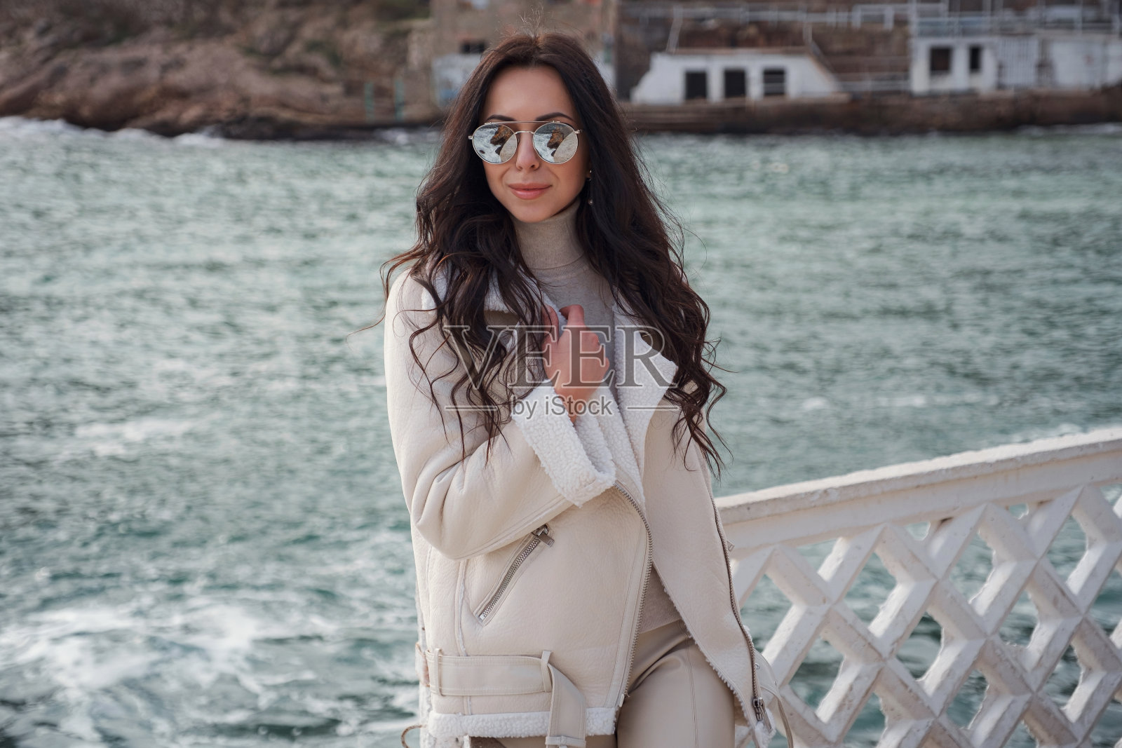 一个穿着米色衣服的女人在一个温暖多风的日子里欣赏着大海的景色。照片摄影图片