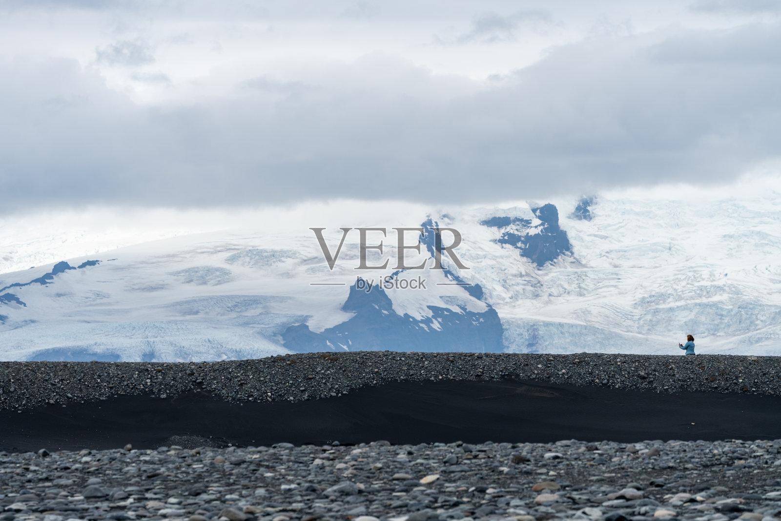 一名女游客在冰岛钻石海滩附近拍摄风景。背景中的大山显示了规模照片摄影图片