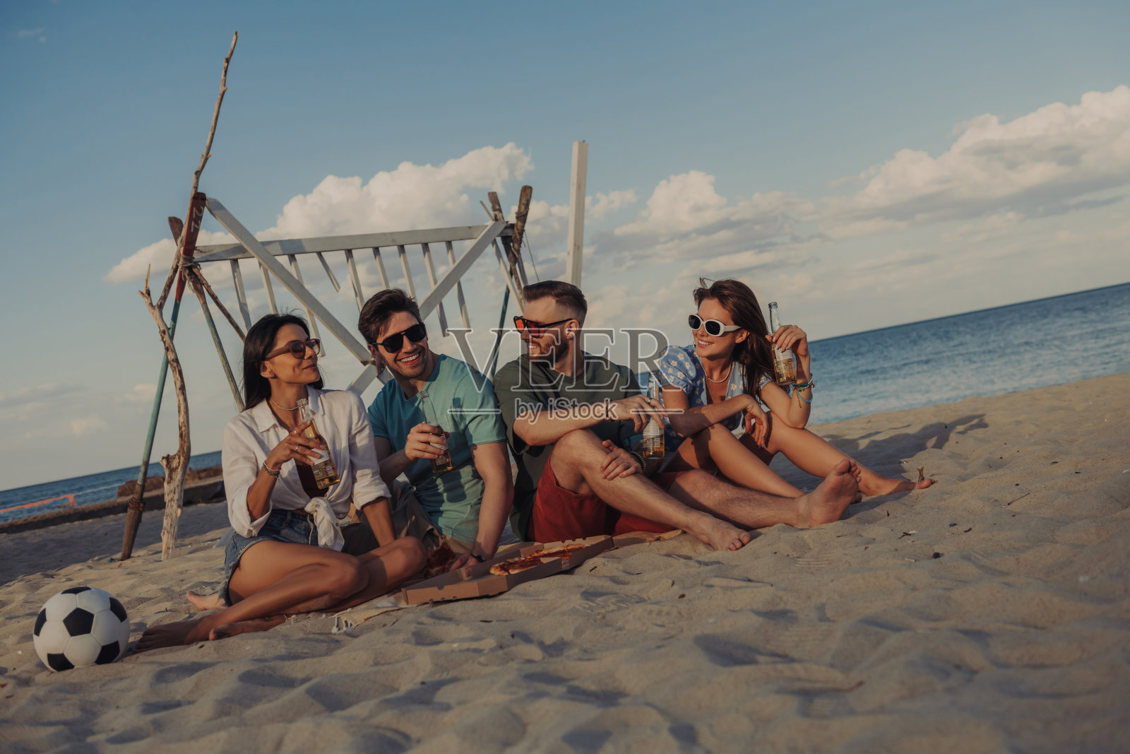 一群兴高采烈的年轻人一起在海滩上享受披萨和啤酒照片摄影图片