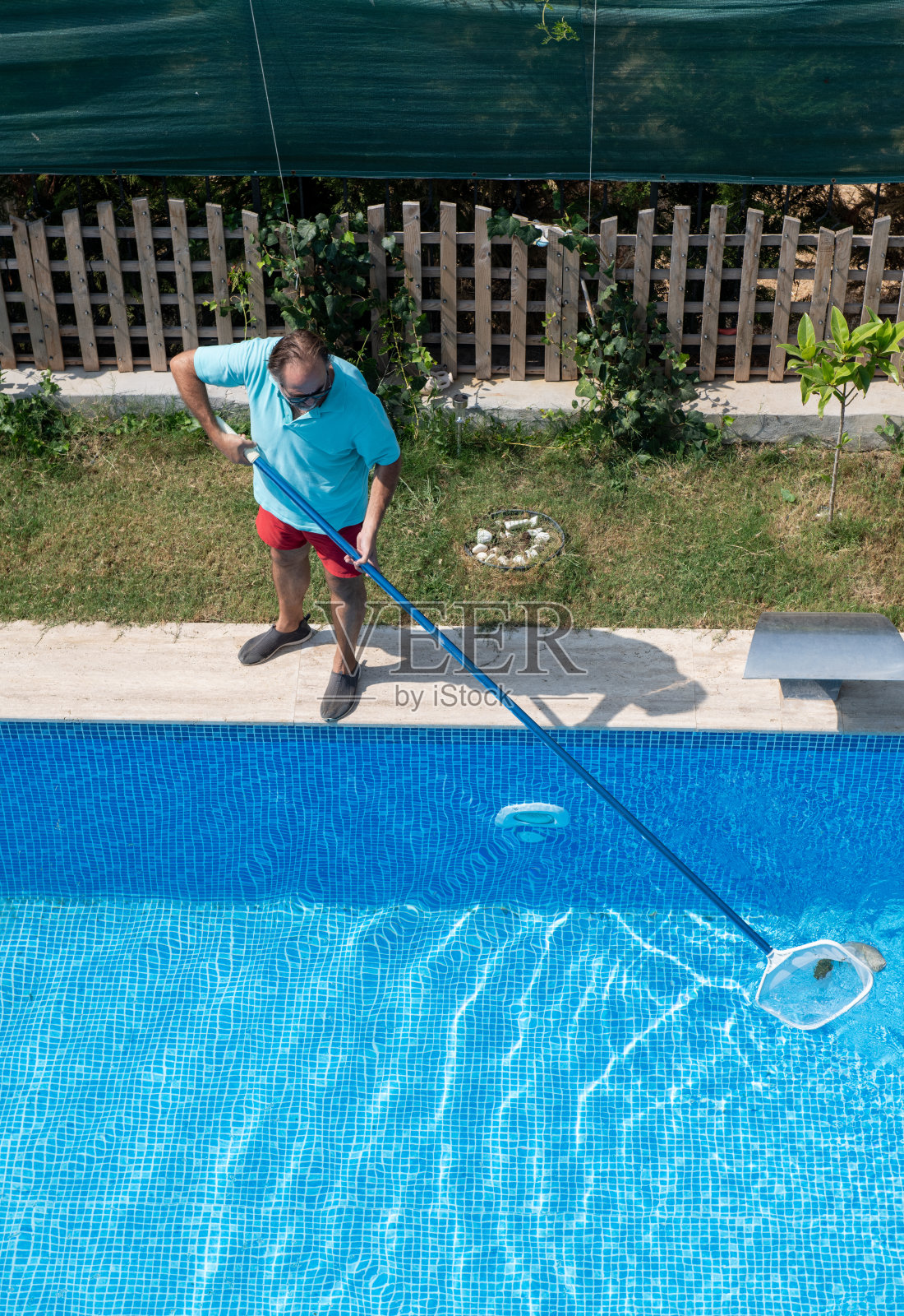 穿着人字拖的男子正在用网清洗游泳池。照片摄影图片