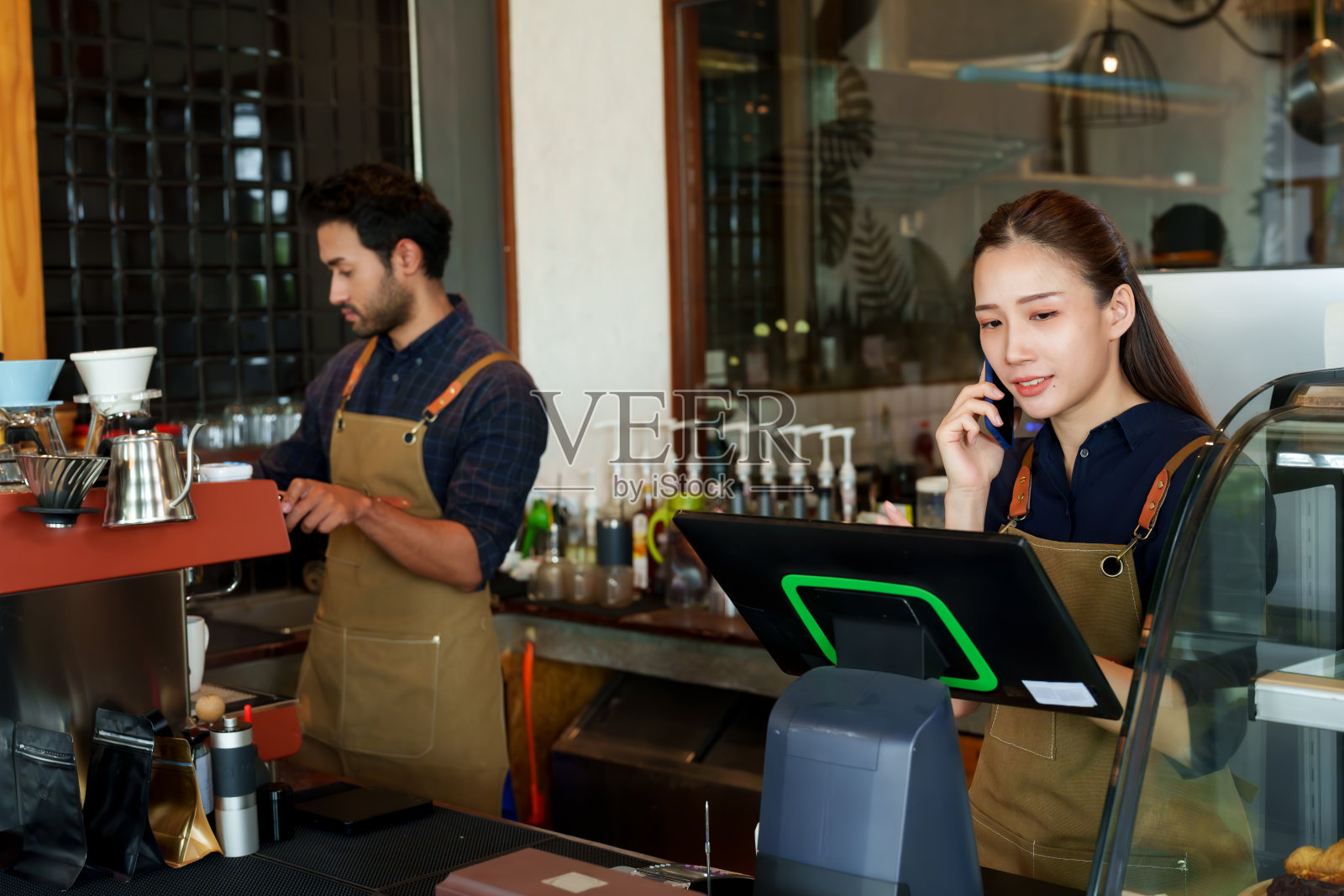 咖啡师夫妇拥有一家小型商业咖啡店。一名亚洲女子站在那里接老顾客的电话订单，一名男子在吧台后面准备煮顾客点的咖啡照片摄影图片