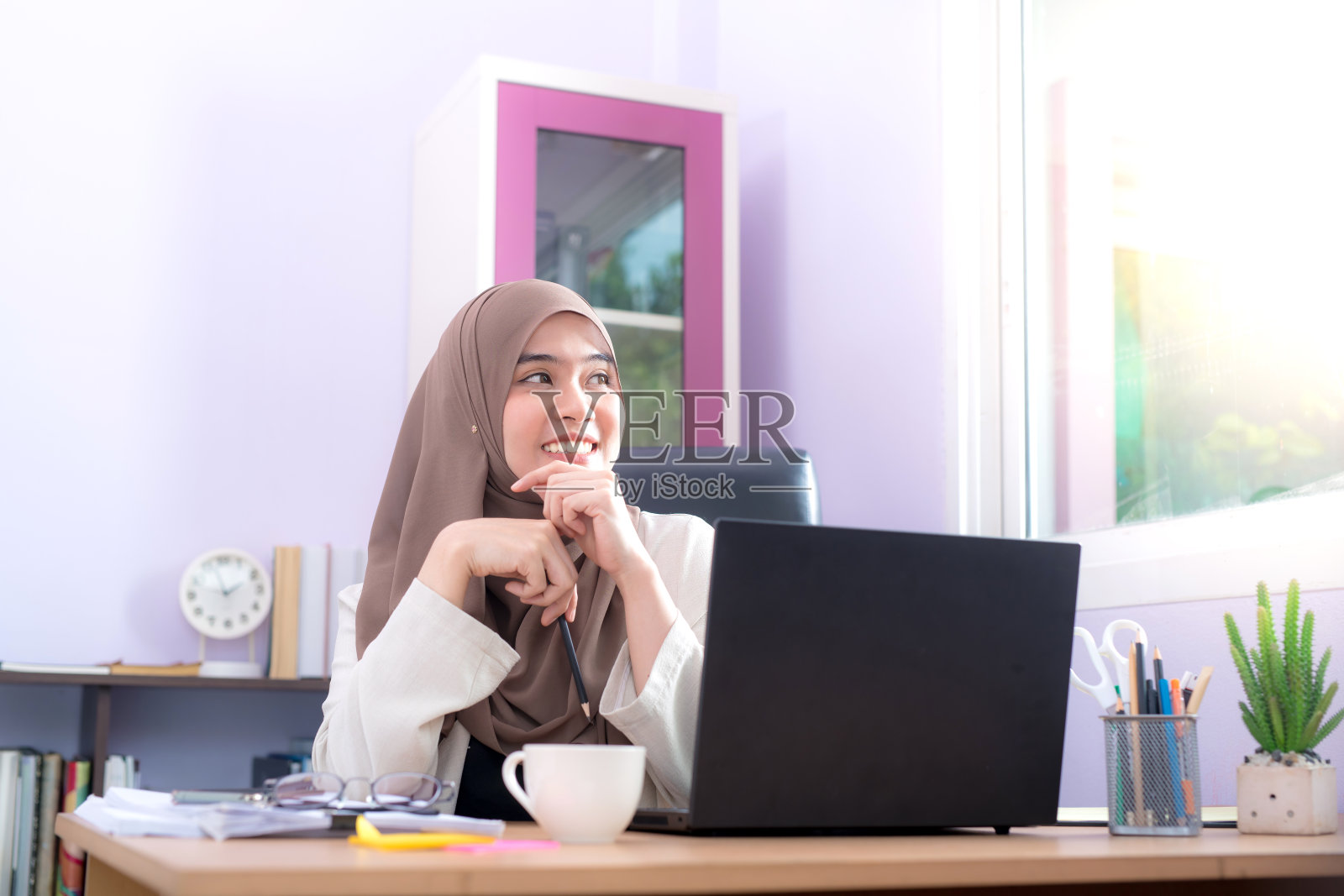 一位亚洲穆斯林妇女的办公室职员坐在她的办公桌前的笔记本电脑前照片摄影图片