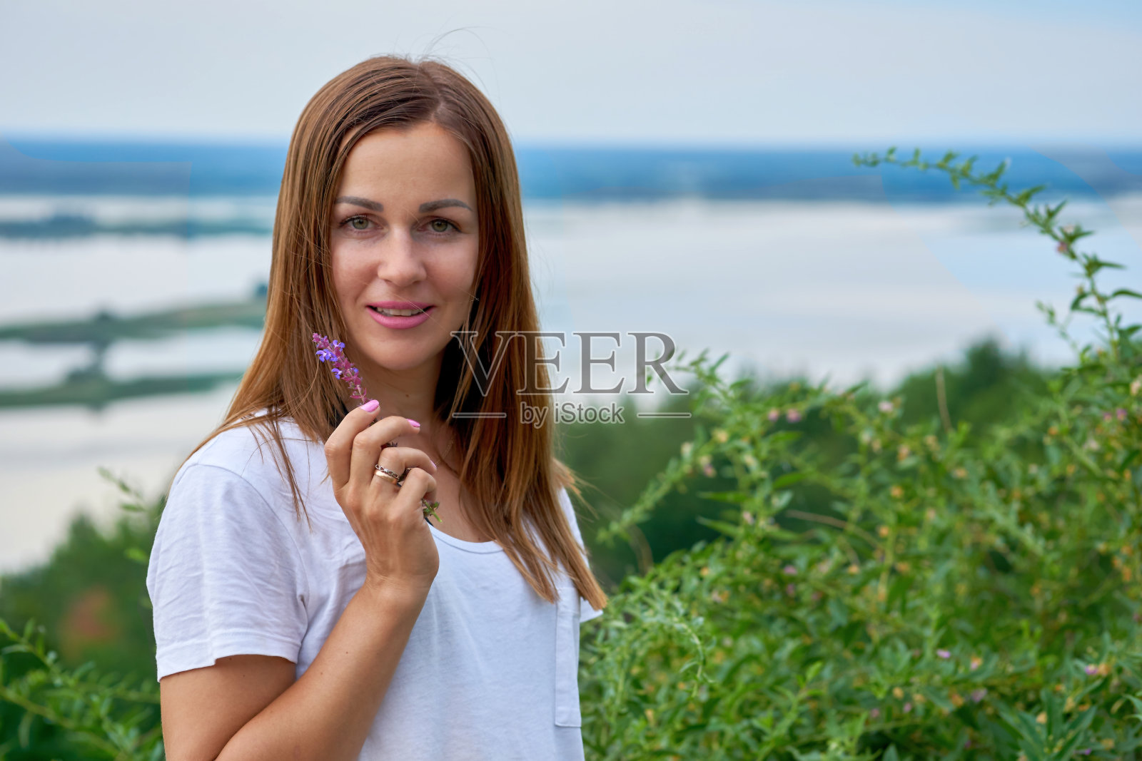 可爱的年轻女子拿着一朵花，在郁郁葱葱的河岸附近照片摄影图片
