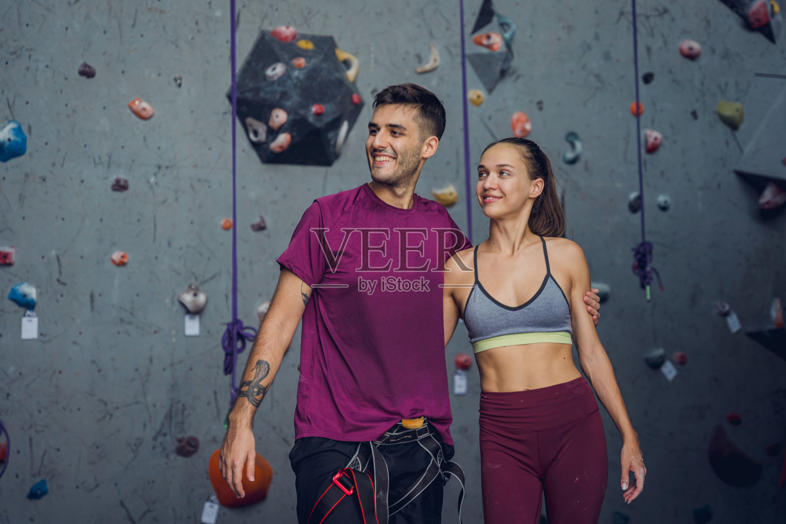 一对强壮的攀登者用彩色的握把和绳索顶着一堵人造墙。照片摄影图片