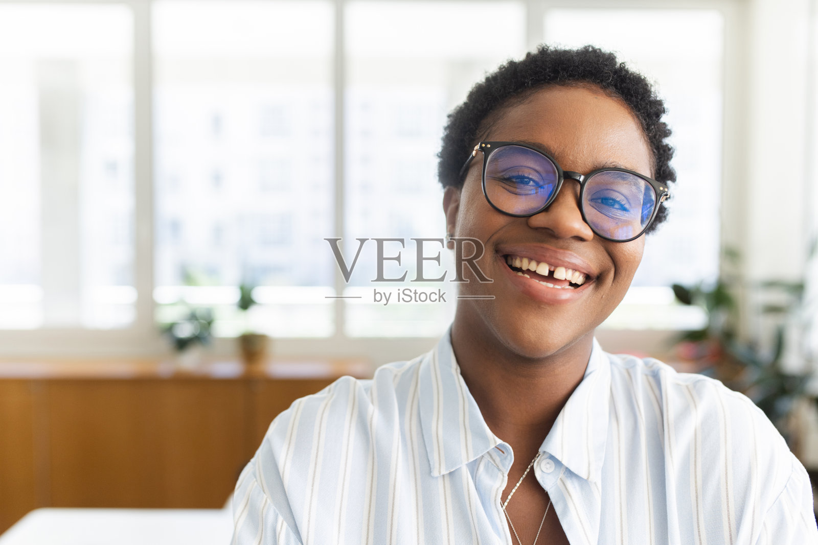一个年轻的非洲女商人的特写，她留着短发，戴着眼镜，笑着独自站在一间现代化的办公室里照片摄影图片