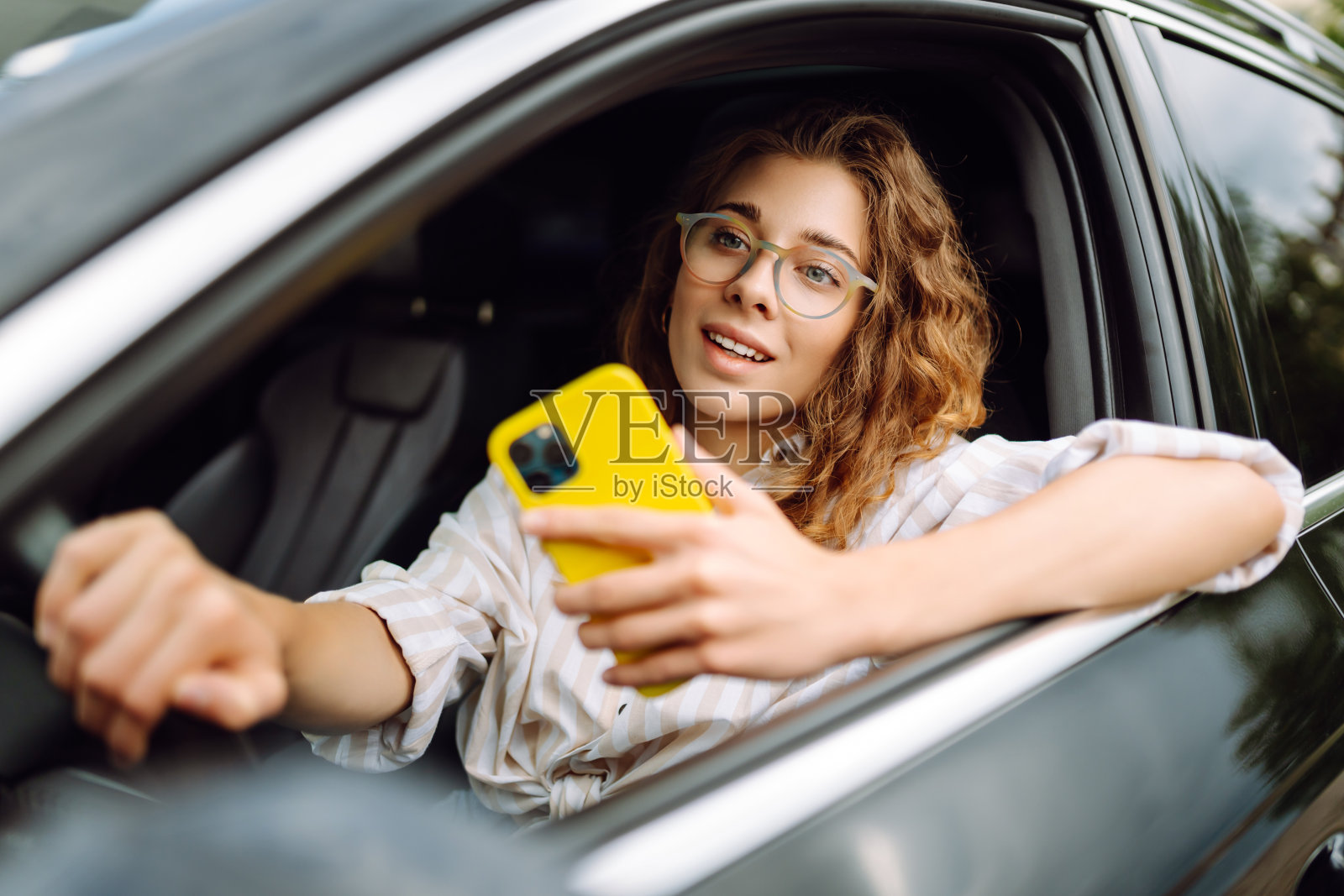 时髦的女人一边开车一边用手机。照片摄影图片