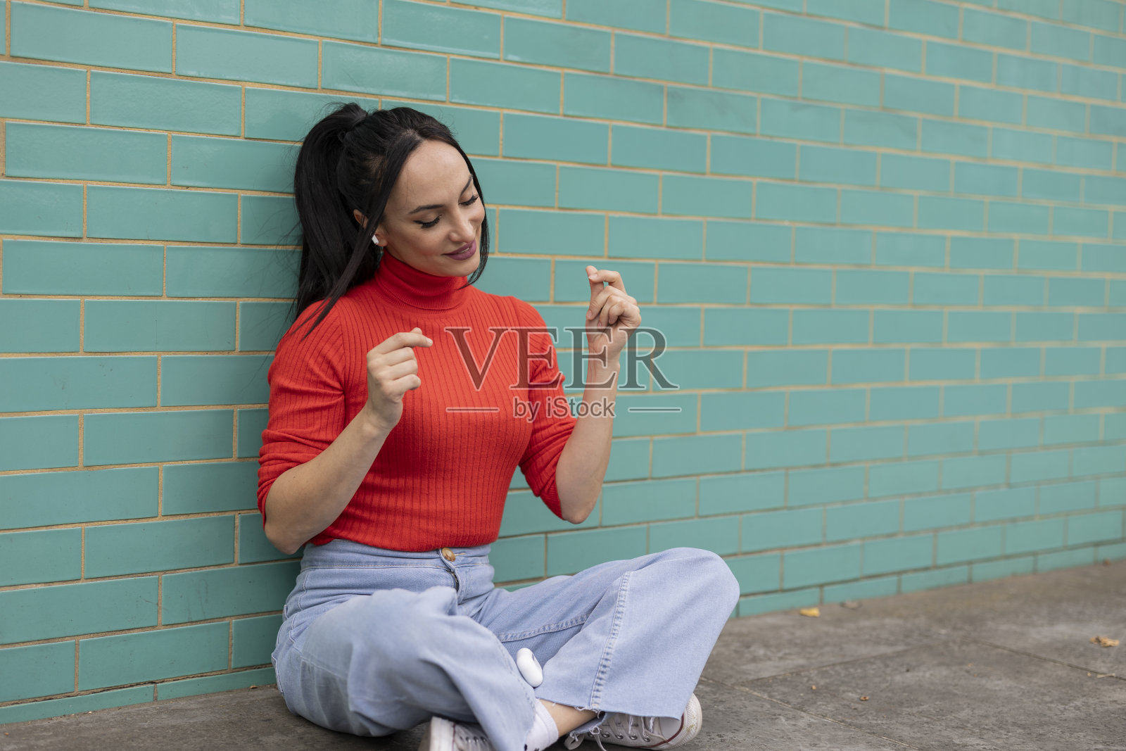 漂亮女人靠在绿松石墙壁上，戴着耳机听音乐照片摄影图片